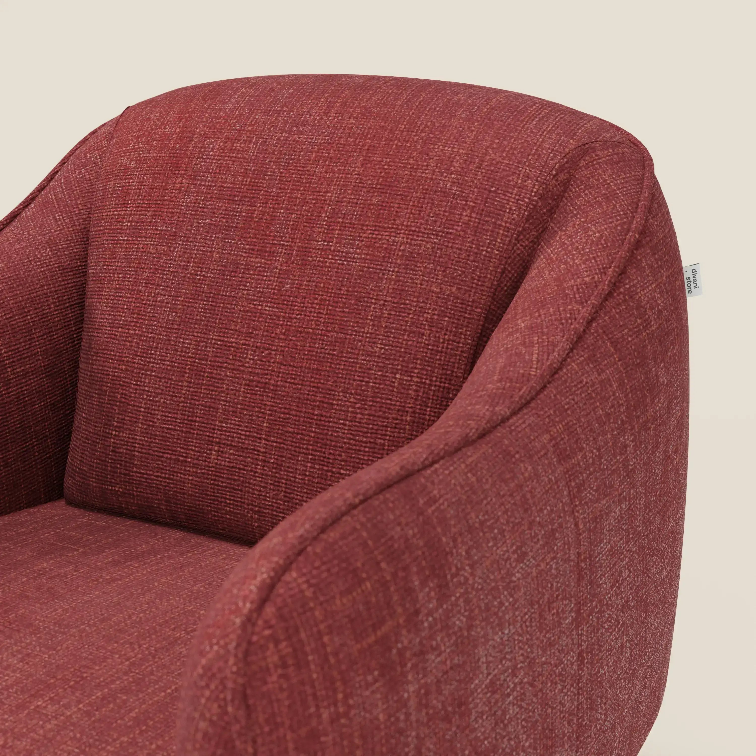 Primo piano di Avela Poltroncina di Divani.Store, rivestita in tessuto impermeabile rosso T06. Presenta uno schienale curvo, braccioli, un design moderno e senza cuciture e una piccola etichetta bianca sul lato posteriore destro. Lo sfondo è bianco sporco.