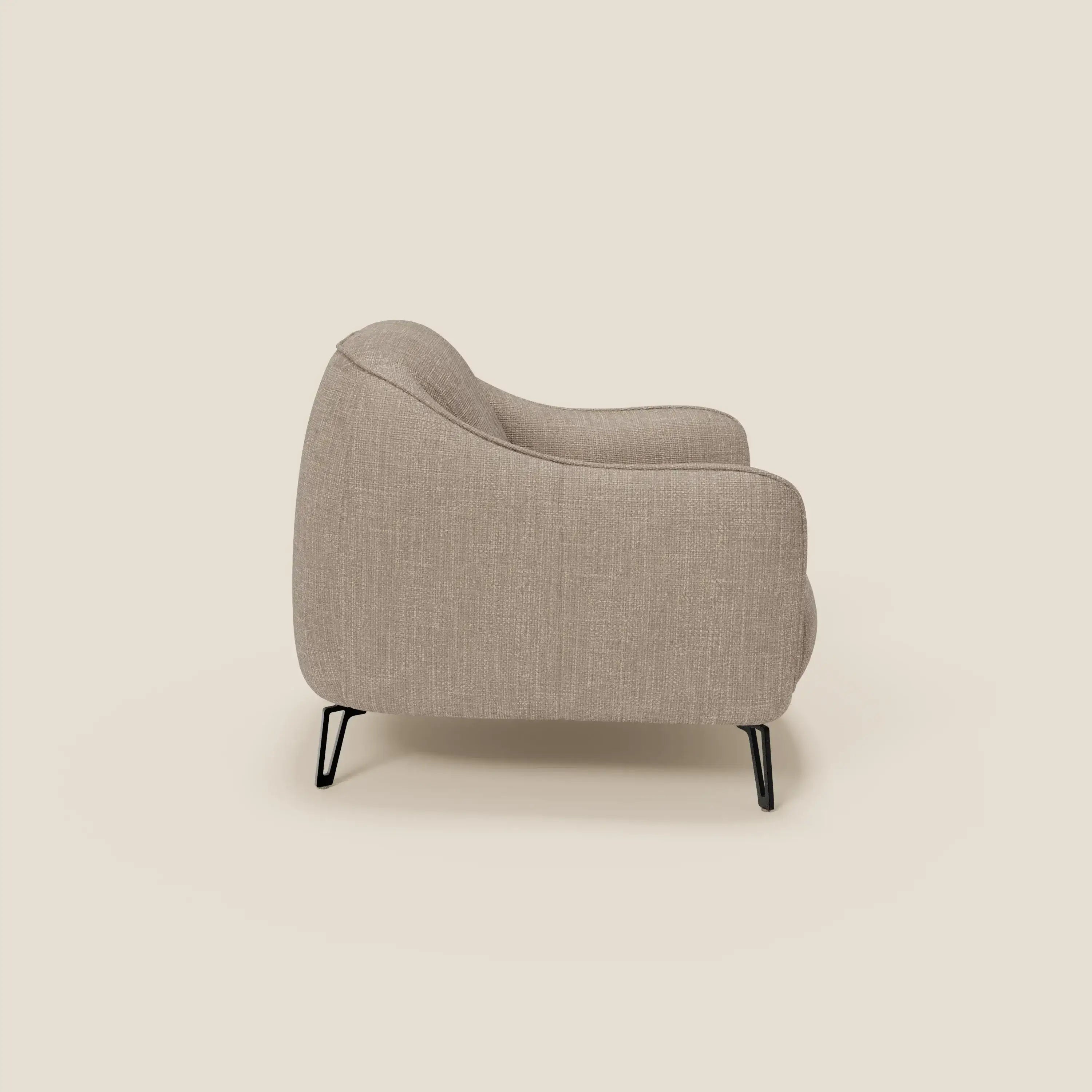 Avela Poltroncina di Divani.Store, vista di lato, presenta un design senza tempo in morbido tessuto tortora T06, resistente all'acqua, con schienale curvo, braccioli, sottili gambe in metallo nero e un look minimalista su uno sfondo crema chiaro.