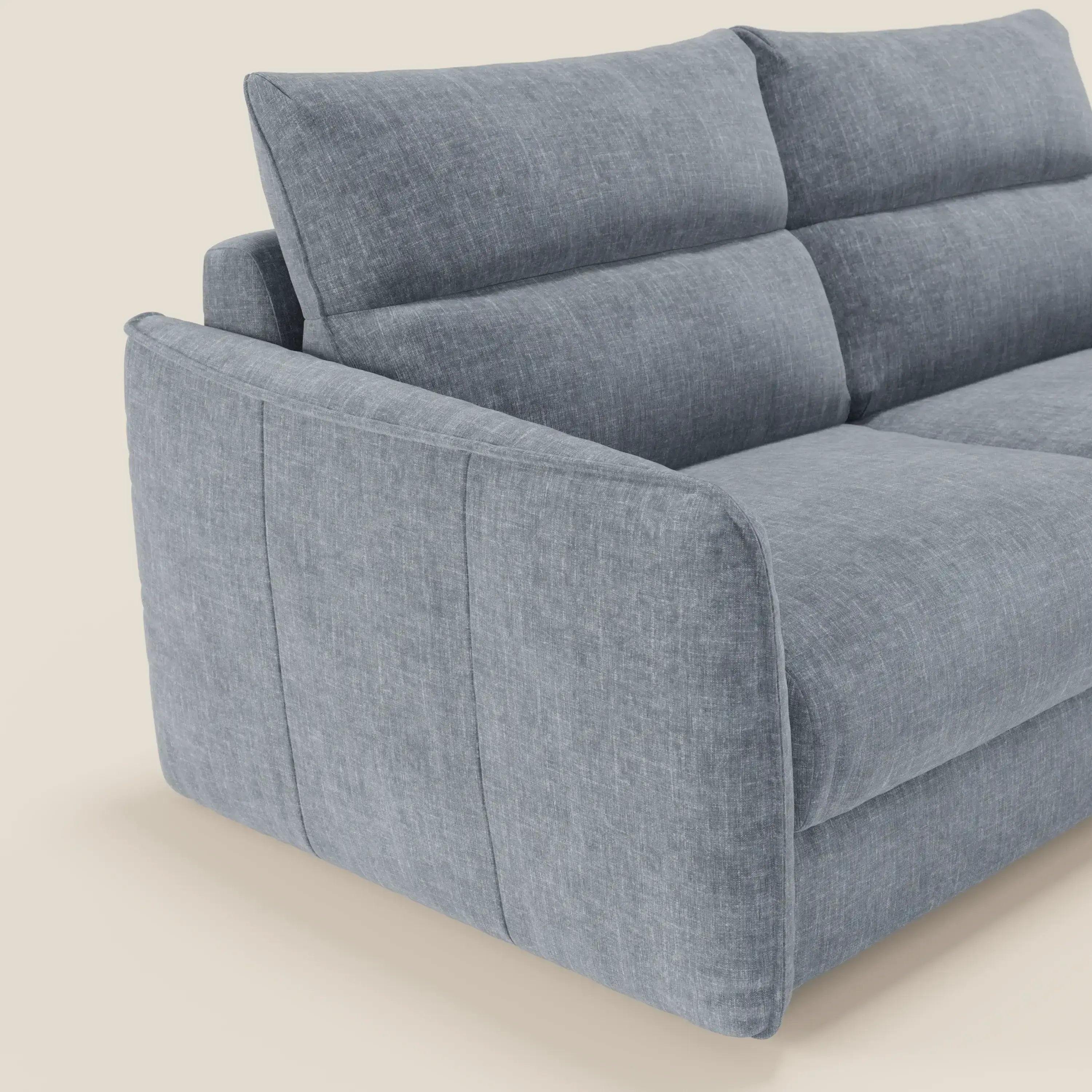 Un primo piano angolato del divano letto Elios di Divani.Store, in tessuto smacchiabile T24 carta da zucchero, con ampi braccioli imbottiti, sedute profonde e schienali segmentati in tessuto morbido che ne evidenziano la struttura elegante.