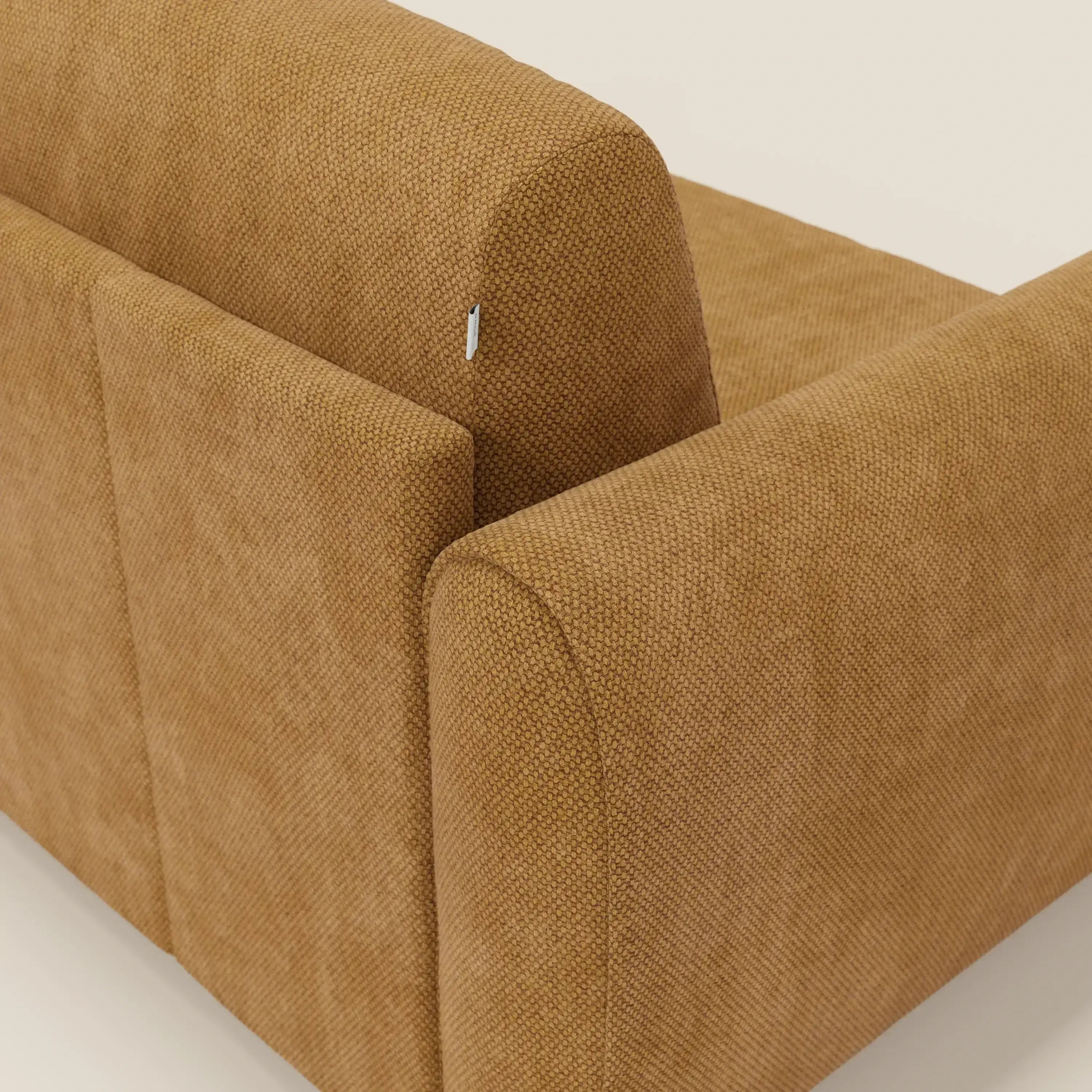 Primo piano dello schienale e del fianco del divano letto moderno Kaleo di Divani.Store in tessuto impermeabile T26 giallo con braccioli arrotondati. Sullo schienale è presente una piccola targhetta bianca; lo sfondo liscio evidenzia il suo design contemporaneo.
