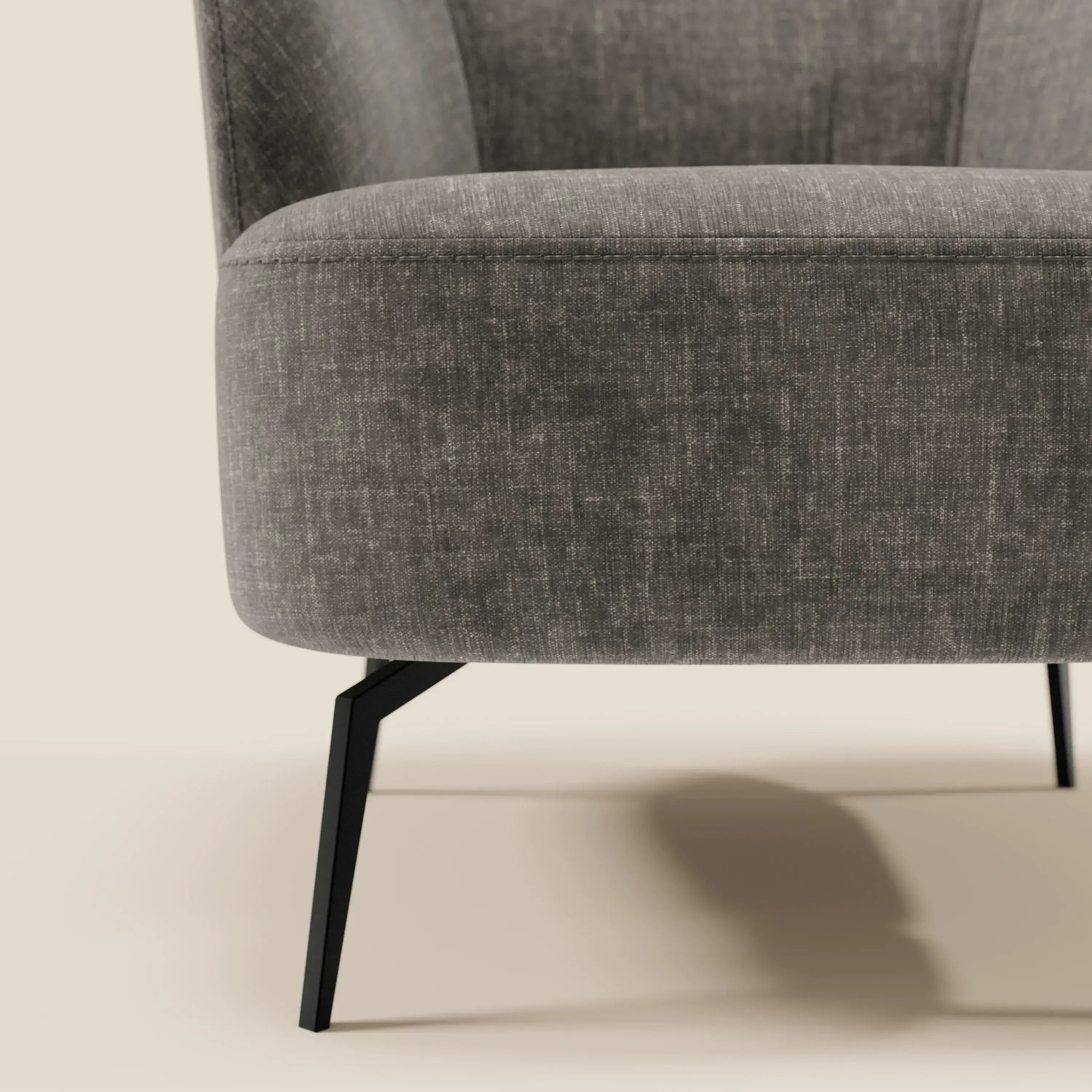 Primo piano della poltroncina Renoa di Divani.Store, caratterizzata da tessuto smacchiabile T24 antracite, eleganti gambe in metallo nero e schienale curvo. La sua moderna eleganza spicca su uno sfondo beige chiaro.