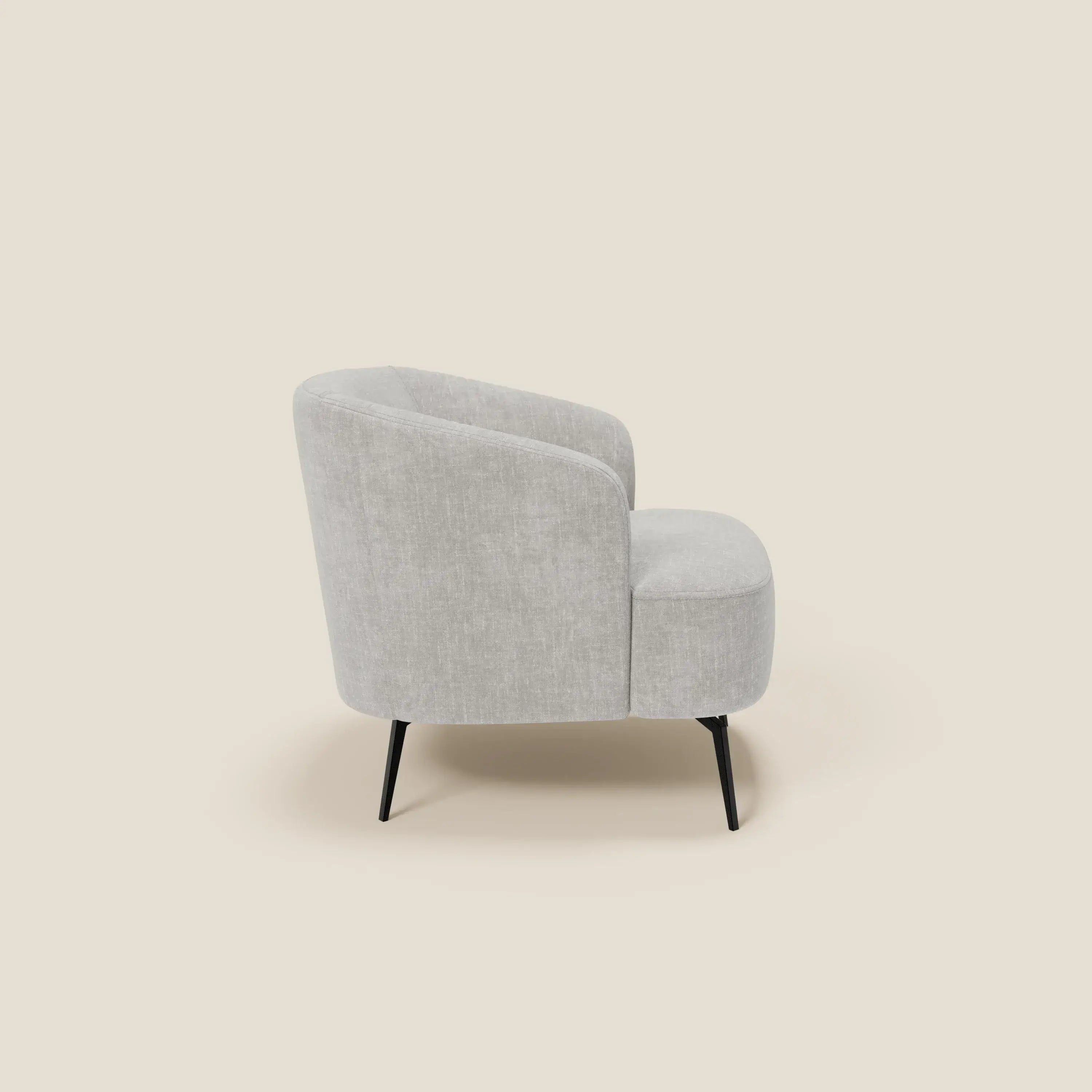La Renoa Poltroncina di Divani.Store, elegante e moderna, è mostrata di lato: schienale e seduta curvi, rivestiti in tessuto smacchiabile T24 grigio chiaro, poggiano su quattro gambe nere sottili su sfondo beige.