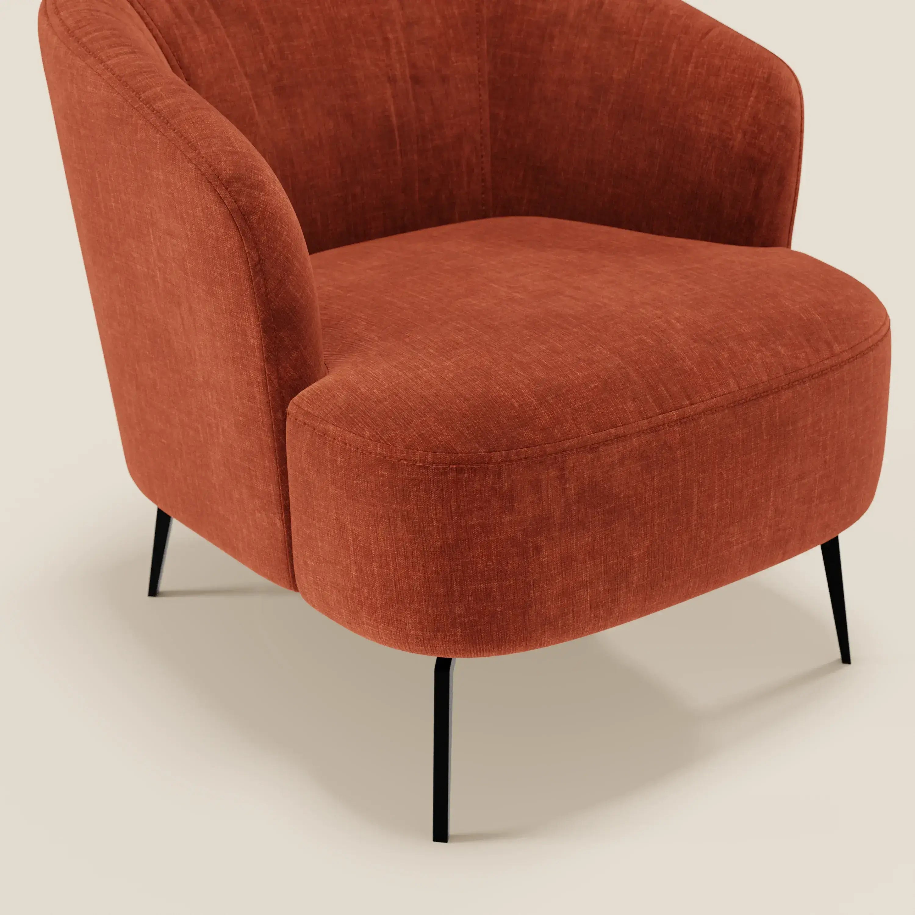 La poltroncina Renoa di Divani.Store, dall'elegante design moderno in tessuto ruggine T24 antimacchia, presenta uno schienale curvo, un'ampia seduta ergonomica e quattro sottili gambe in metallo nero; solo una parte è visibile su uno sfondo beige chiaro.