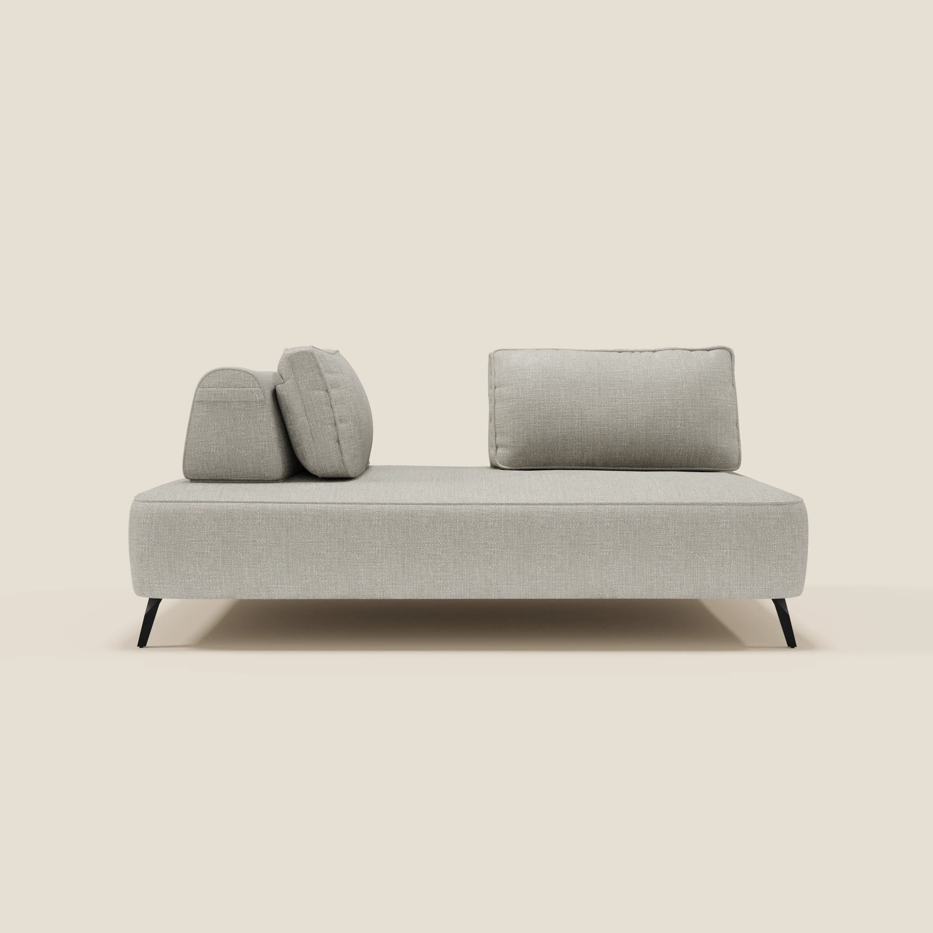Un moderno divano imbottito grigio chiaro con tre cuscini di schienale poggia su sottili gambe nere su un semplice sfondo beige. Il design è minimalista ed elegante, con linee pulite e senza braccioli.