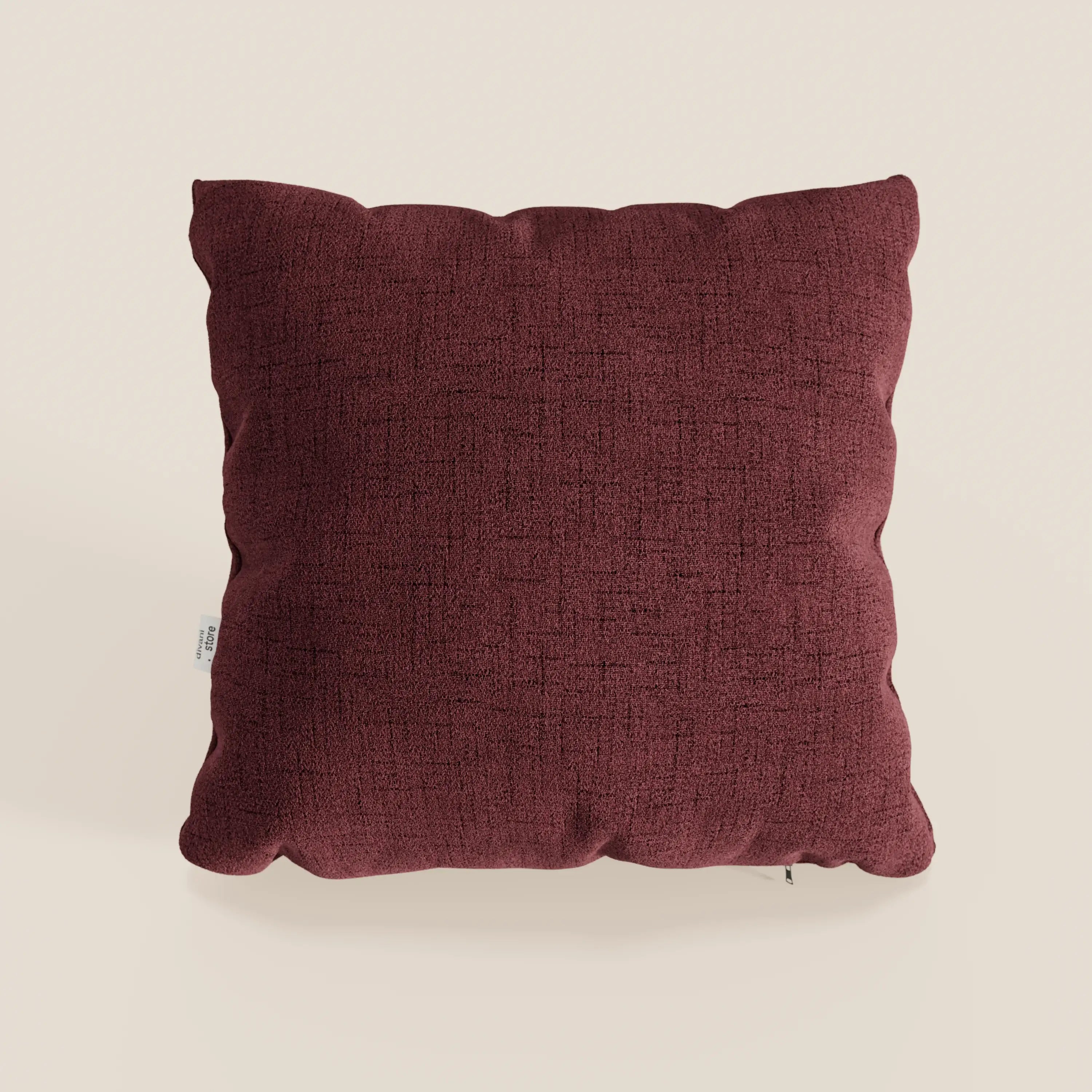 Il cuscino Felis di Divani.Store in rosso T03 è un cuscino quadrato, marrone, impermeabile, con tessuto morbido, superficie strutturata, design minimalista, angoli arrotondati, cuciture a vista e una piccola etichetta bianca sul lato sinistro su sfondo beige.