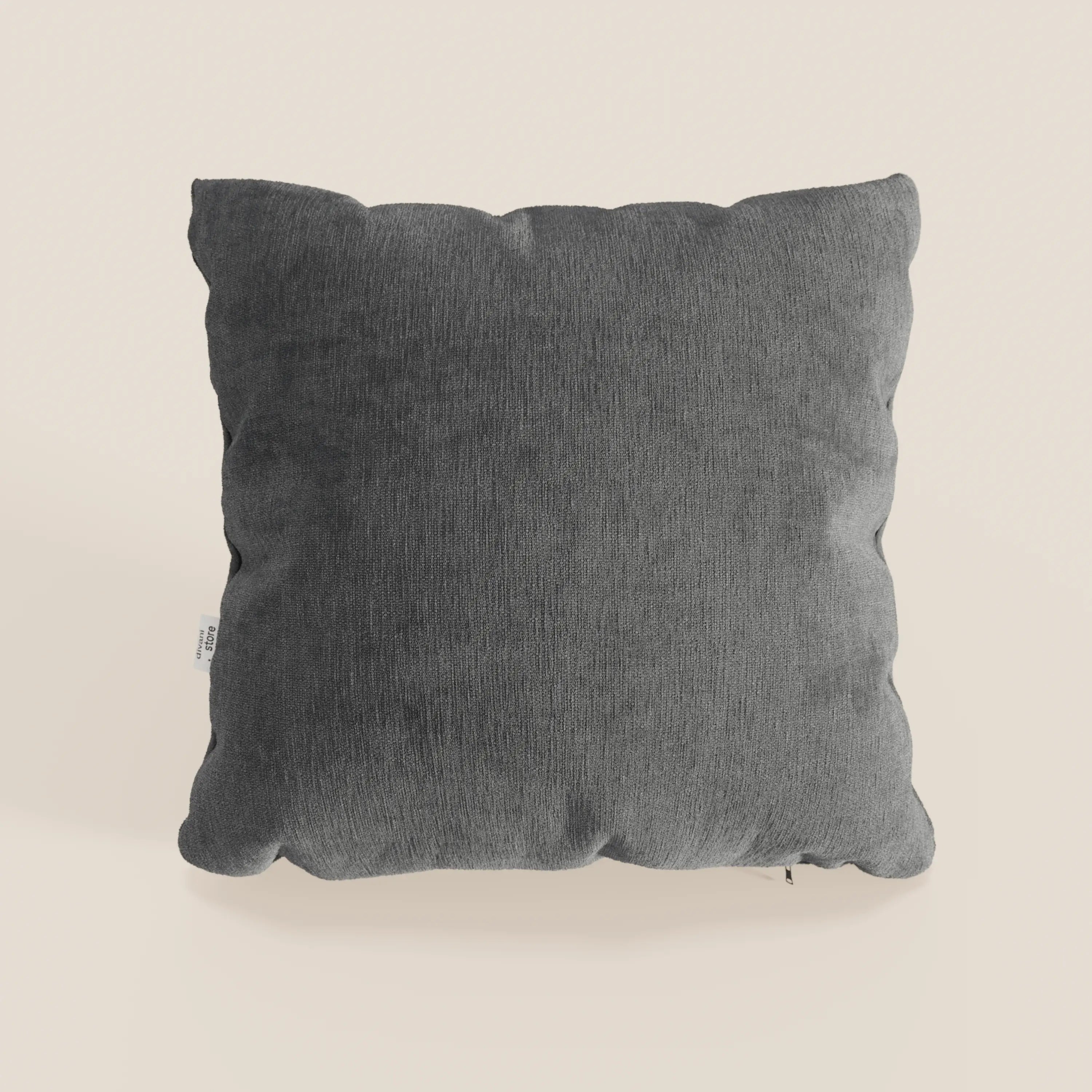 Il cuscino Bolero di Divani.Store è presentato in grigio scuro, con un tessuto T31 morbido e testurizzato, resistente alle macchie, all'acqua e agli strizzacervelli; ha bordi felpati leggermente irregolari e un'etichetta di manutenzione bianca sulla sinistra.