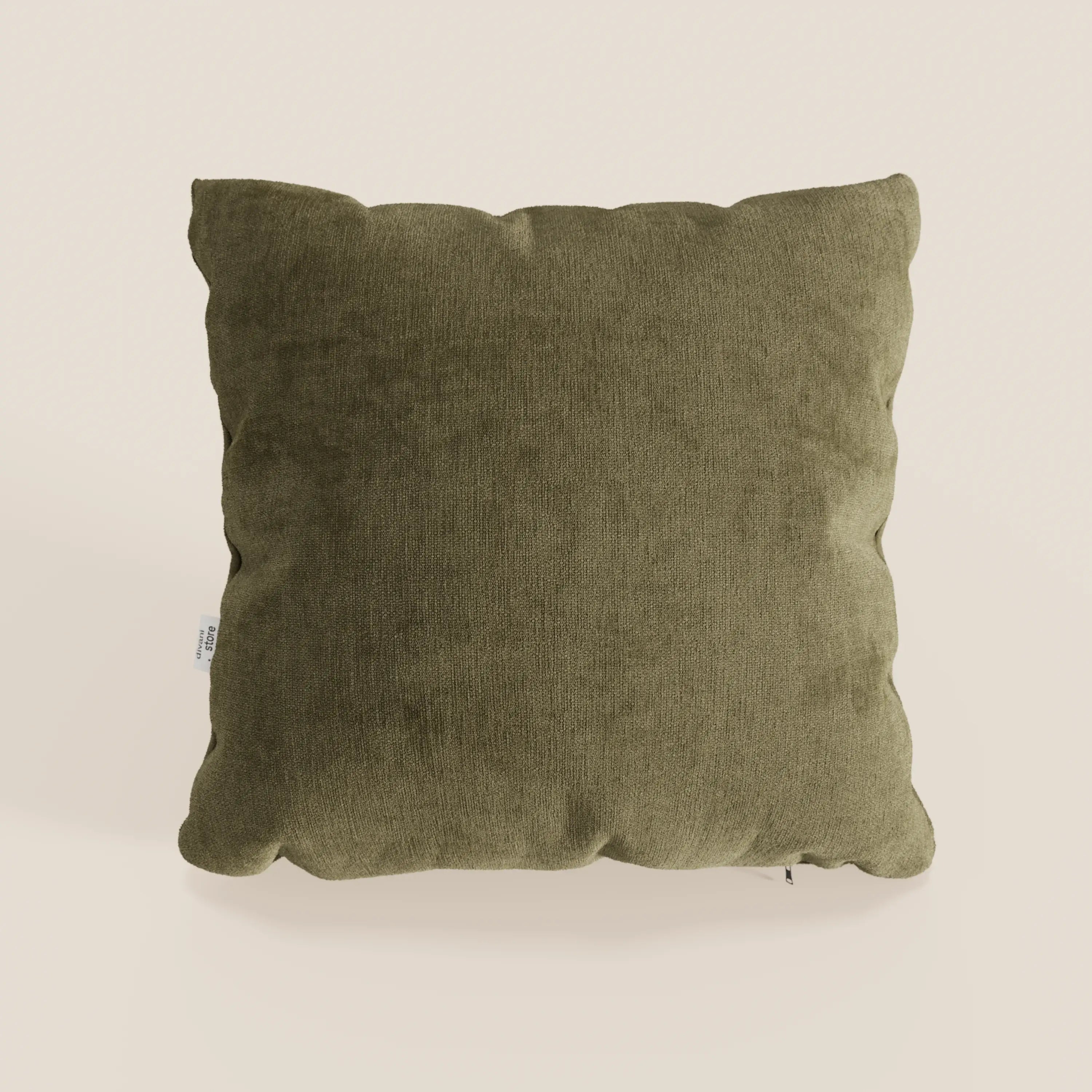 Un cuscino Bolero quadrato verde oliva di Divani.Store, realizzato in morbido tessuto T31 antimacchia, impermeabile e non restringente, si staglia su un semplice sfondo beige. Gli angoli leggermente arrotondati e una piccola etichetta bianca aggiungono un fascino discreto.