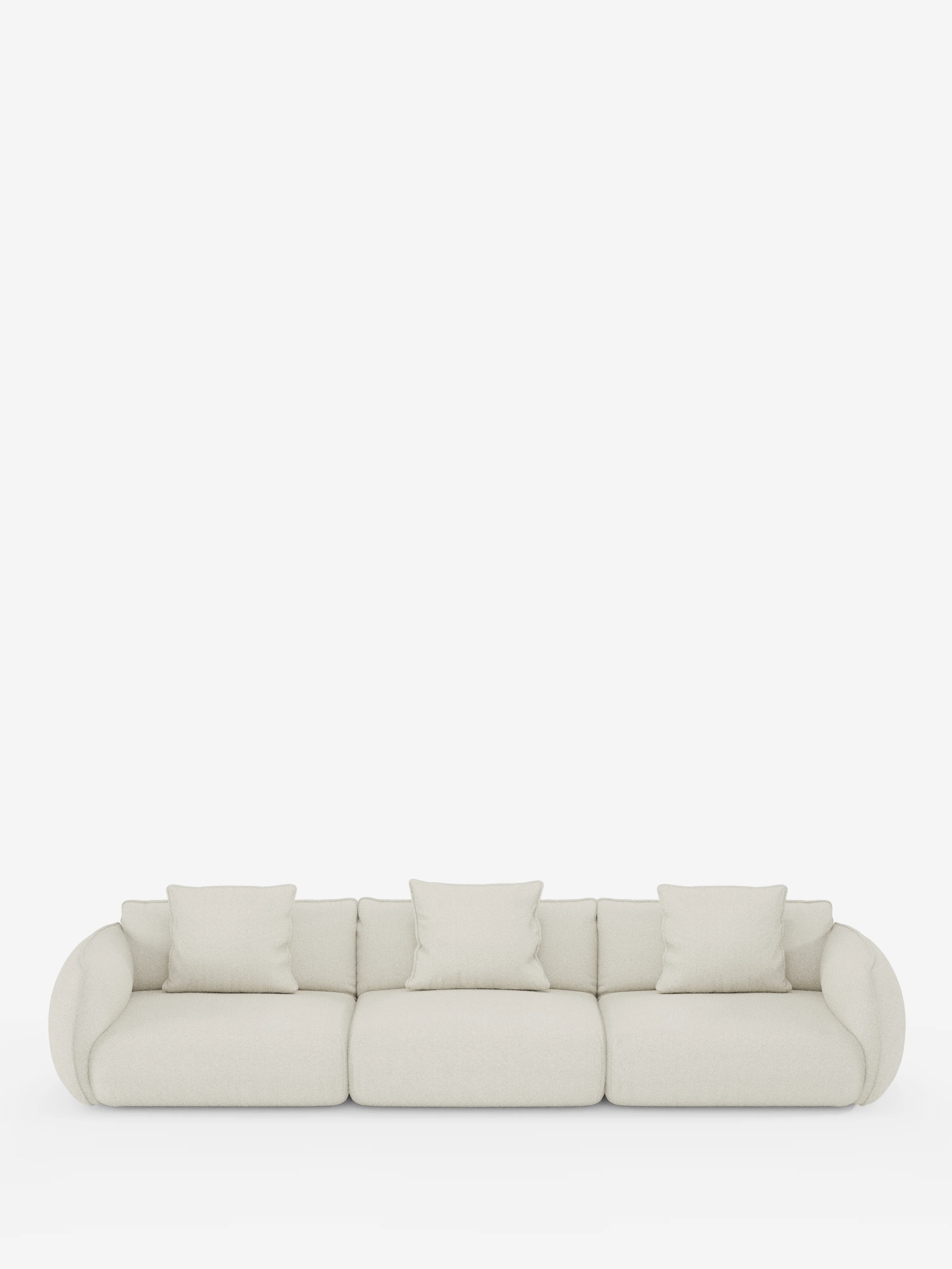 Un moderno divano modulare Nimbus a 3 posti di Divani.Store, rivestito in tessuto T33 effetto cotone resistente alle macchie, color beige chiaro, caratterizzato da braccioli arrotondati e quattro cuscini quadrati coordinati, su uno sfondo bianco a tinta unita.