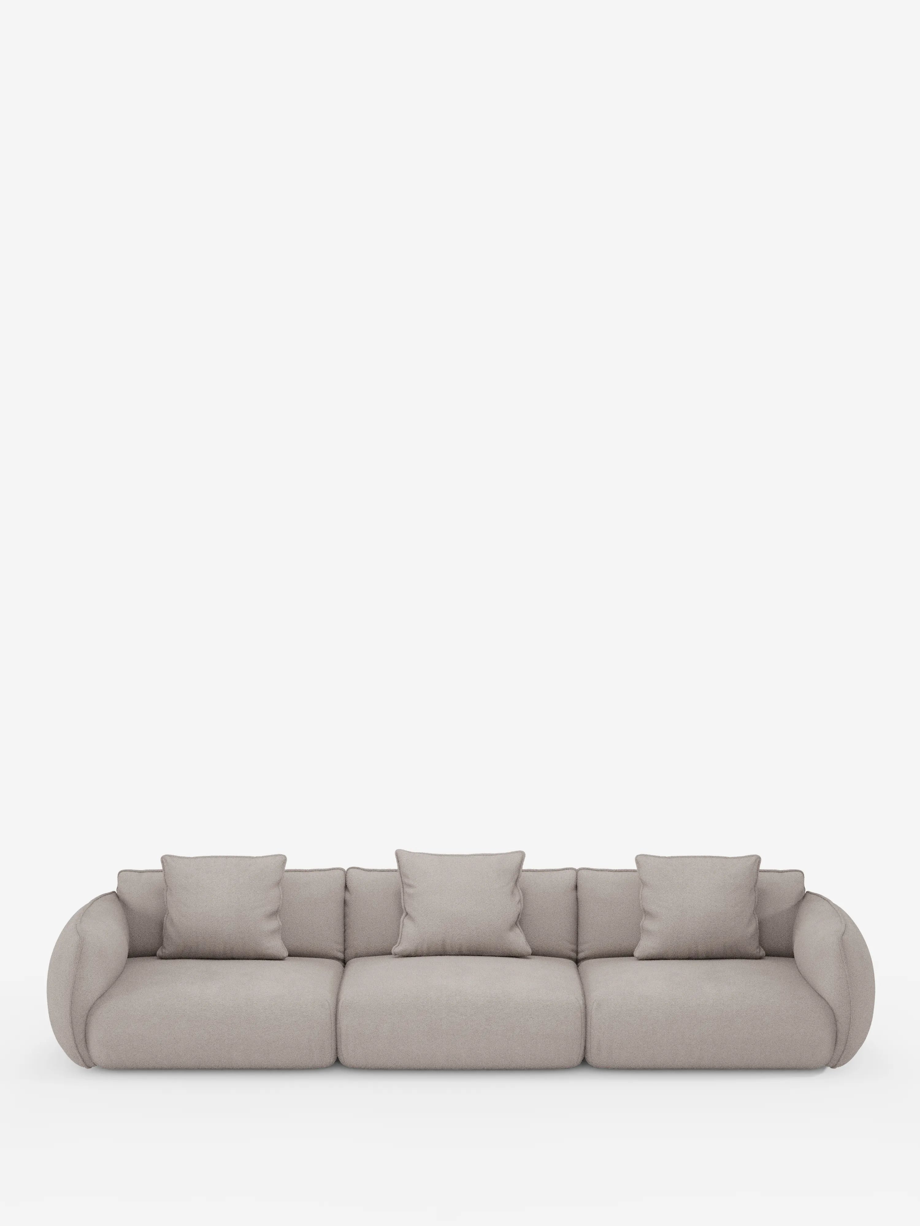 Un moderno divano modulare Nimbus a 3 posti di Divani.Store, rivestito in tessuto T33 beige chiaro smacchiabile effetto cotone. Questo elegante divano è dotato di tre cuscini di seduta e quattro cuscini quadrati abbinati, con braccioli arrotondati e schienale basso. Si presenta su una base bianca liscia, senza gambe visibili né elementi decorativi.