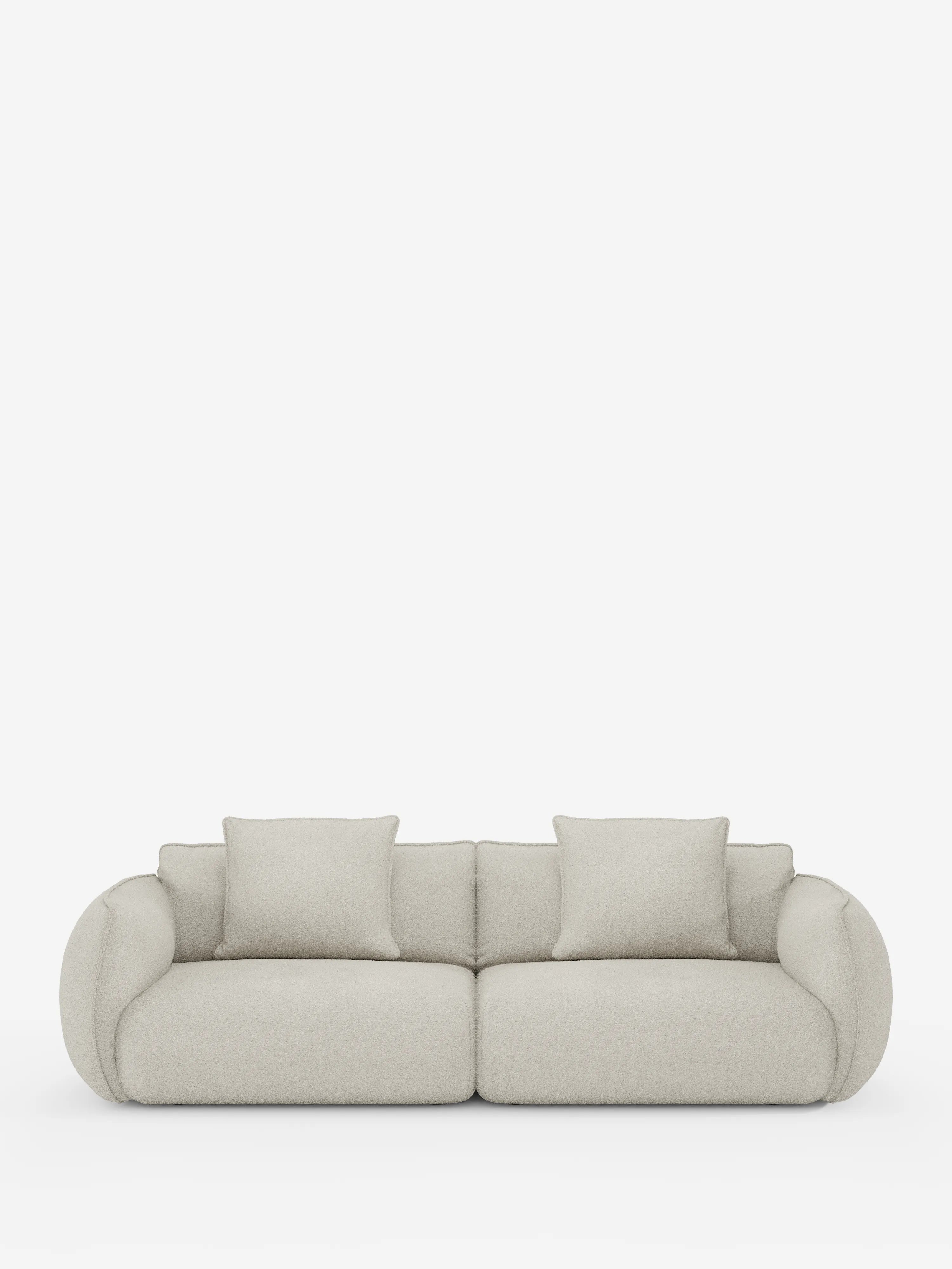 Un moderno divano modulare a 3 posti Nimbus di Divani.Store, rivestito in tessuto effetto cotone (t33) di colore beige chiaro e resistente alle macchie, dotato di due ampi cuscini di seduta e due cuscini dello schienale. I braccioli arrotondati e di grandi dimensioni conferiscono al divano un aspetto lussuoso e accogliente. Il divano è esposto su uno sfondo bianco a tinta unita.