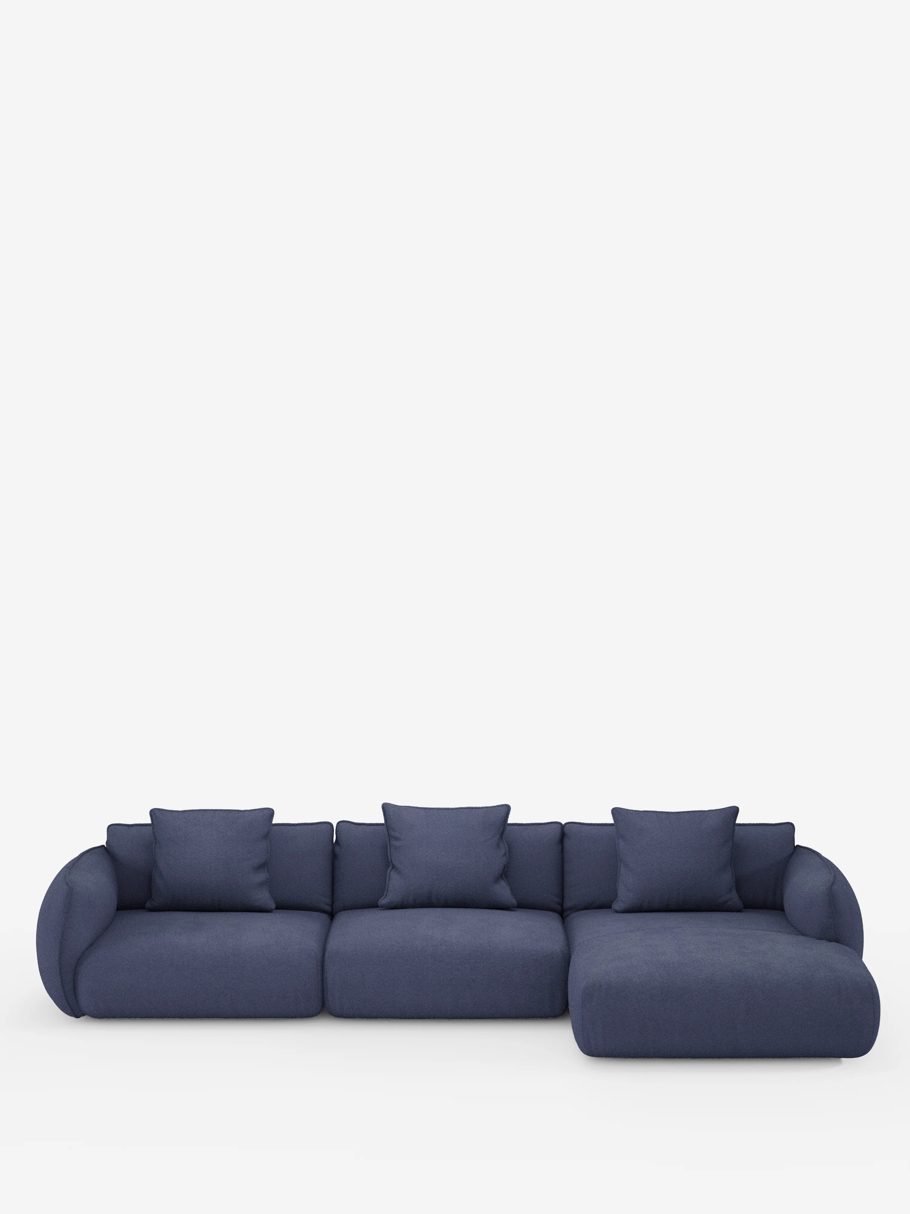 Un divano angolare Nimbus contemporaneo color blu navy con penisola componibile, rivestito in morbido tessuto effetto cotone lavabile T33 di Divani.Store, caratterizzato da braccioli arrotondati, tre cuscini di seduta, una chaise longue sul lato destro e quattro cuscini quadrati coordinati, il tutto su uno sfondo bianco a tinta unita.