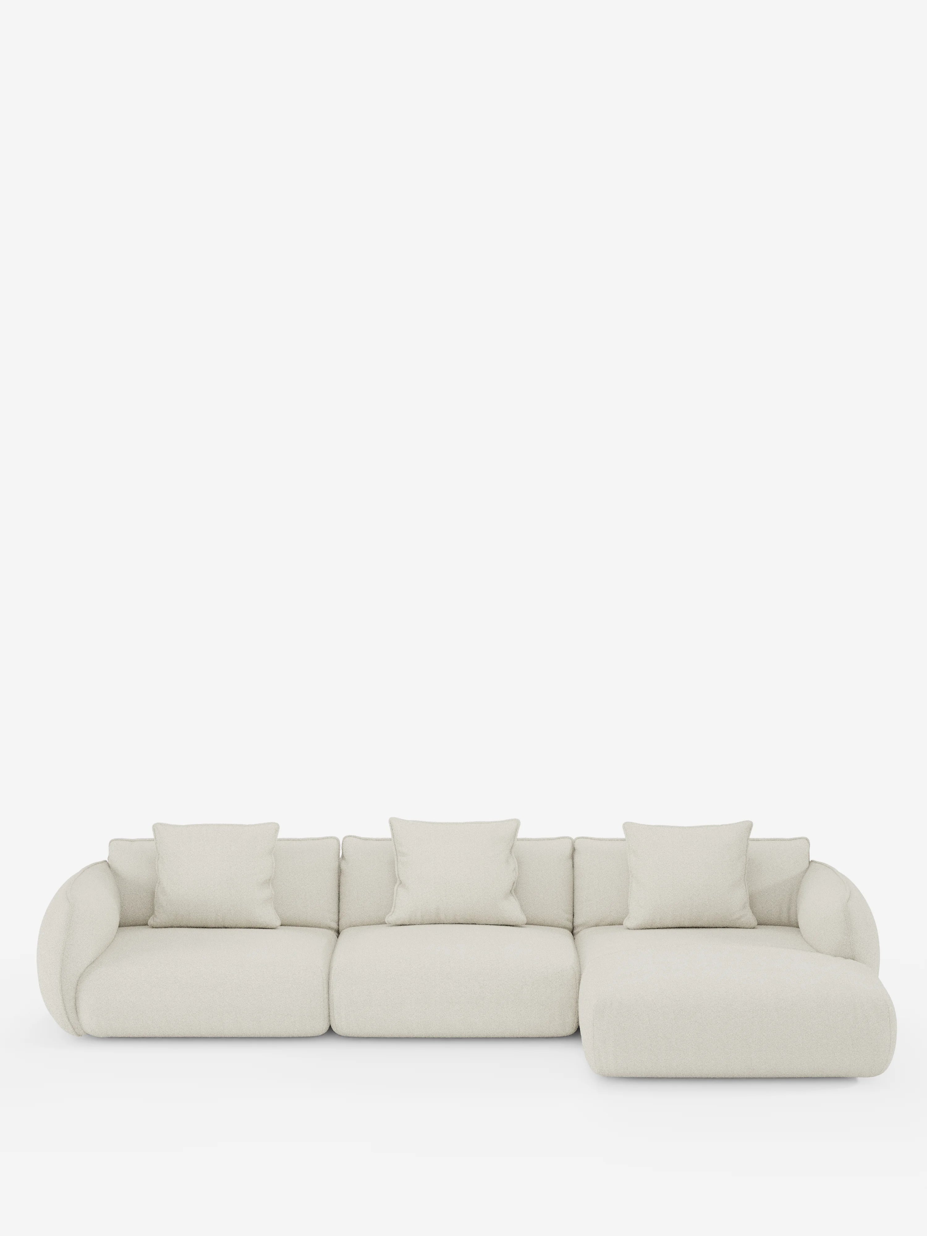Un divano angolare con penisola componibile Nimbus, dal design contemporaneo e minimalista, firmato Divani.Store, rivestito in tessuto T33 effetto cotone color beige chiaro, antimacchia. Il divano comprende tre sezioni di seduta, quattro cuscini coordinati e una chaise longue sul lato destro (penisola), il tutto presentato su uno sfondo bianco. I bordi arrotondati e il design morbido creano un'estetica accogliente.