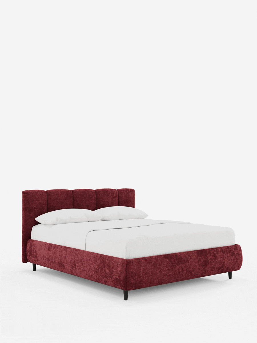 Il letto imbottito ARKAM con contenitore e testiera a lavorazione verticale è un letto imbottito di colore rosso scuro con testiera cucita, cuscini bianchi e lenzuola bianche, poggiato su sottili piedini neri su uno sfondo grigio chiaro.