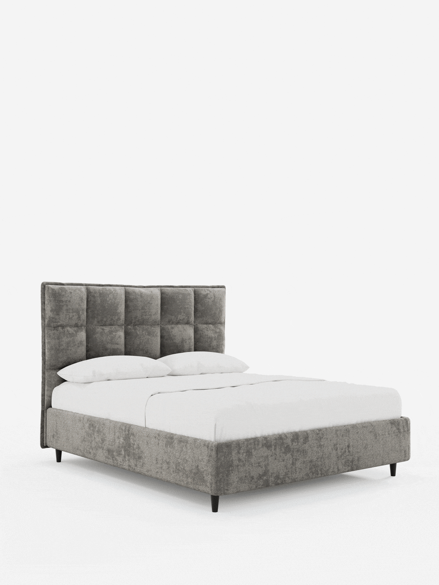 Il letto imbottito AURO con contenitore e testiera alta capitonné in ciniglia Oeko-Tex® è un letto imbottito grigio con una testiera alta a pannelli, una struttura dal profilo basso, biancheria da letto di un bianco brillante e piccole gambe affusolate di colore scuro su sfondo bianco.
