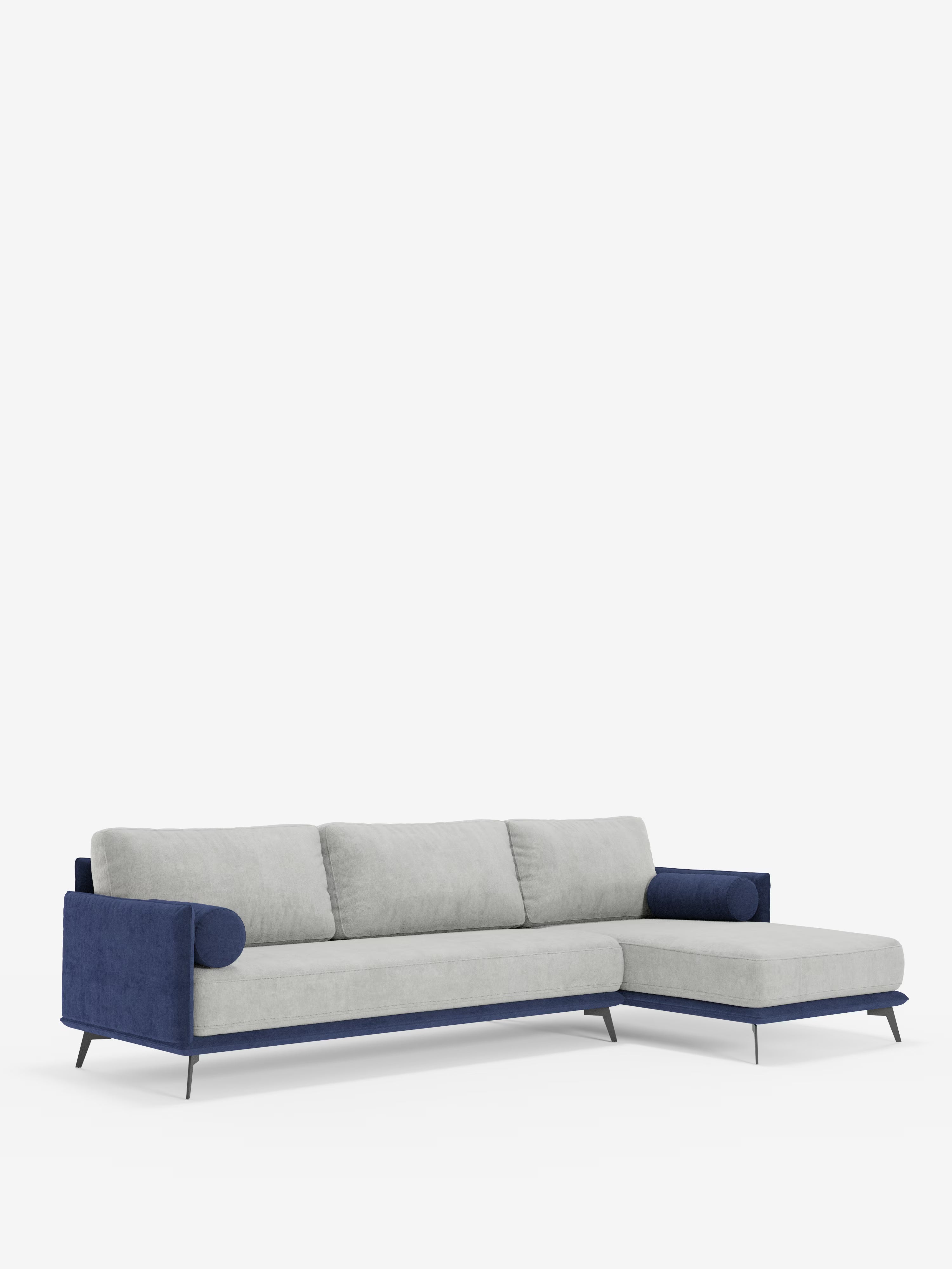 Un divano angolare bicolore contemporaneo della linea Basalto con penisola e base in metallo di Divani.Store, caratterizzato da cuscini in tessuto T31 grigio chiaro smacchiabile con morbidi schienali imbottiti in piuma e braccioli, base e dettagli laterali a contrasto in blu scuro. La penisola bicolore, posizionata sul lato destro, poggia su sottili gambe in metallo nero. Sullo sfondo di un bianco semplice, il design risulta minimalista e moderno.
