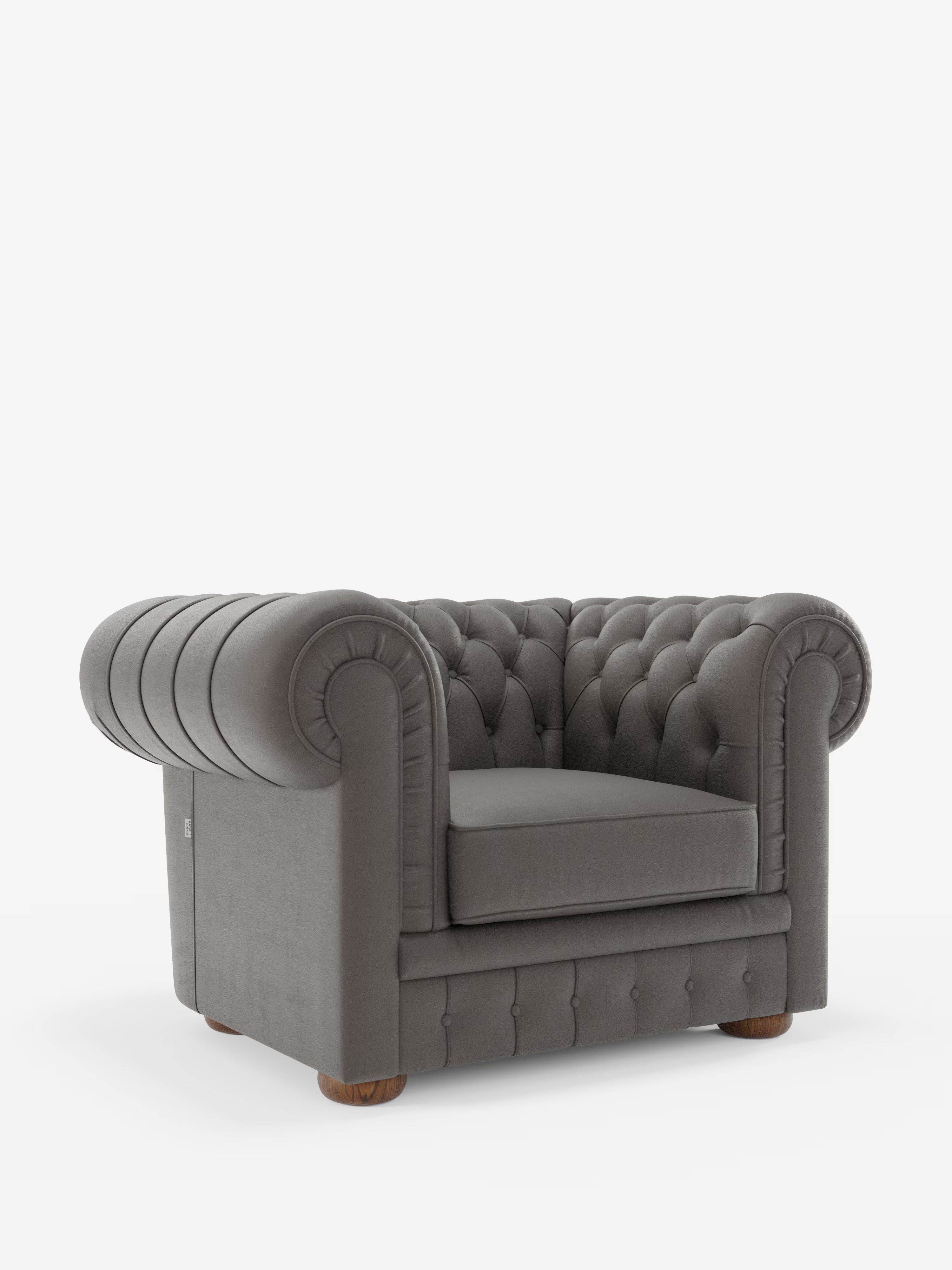 Una poltrona Chester in vera pelle spessorata con capitonné artigianale di Divani.Store, caratterizzata da una finitura grigia scura con capitonné, braccioli arrotondati, profondi bottoni decorativi e piedini in legno, su uno sfondo bianco a tinta unita.