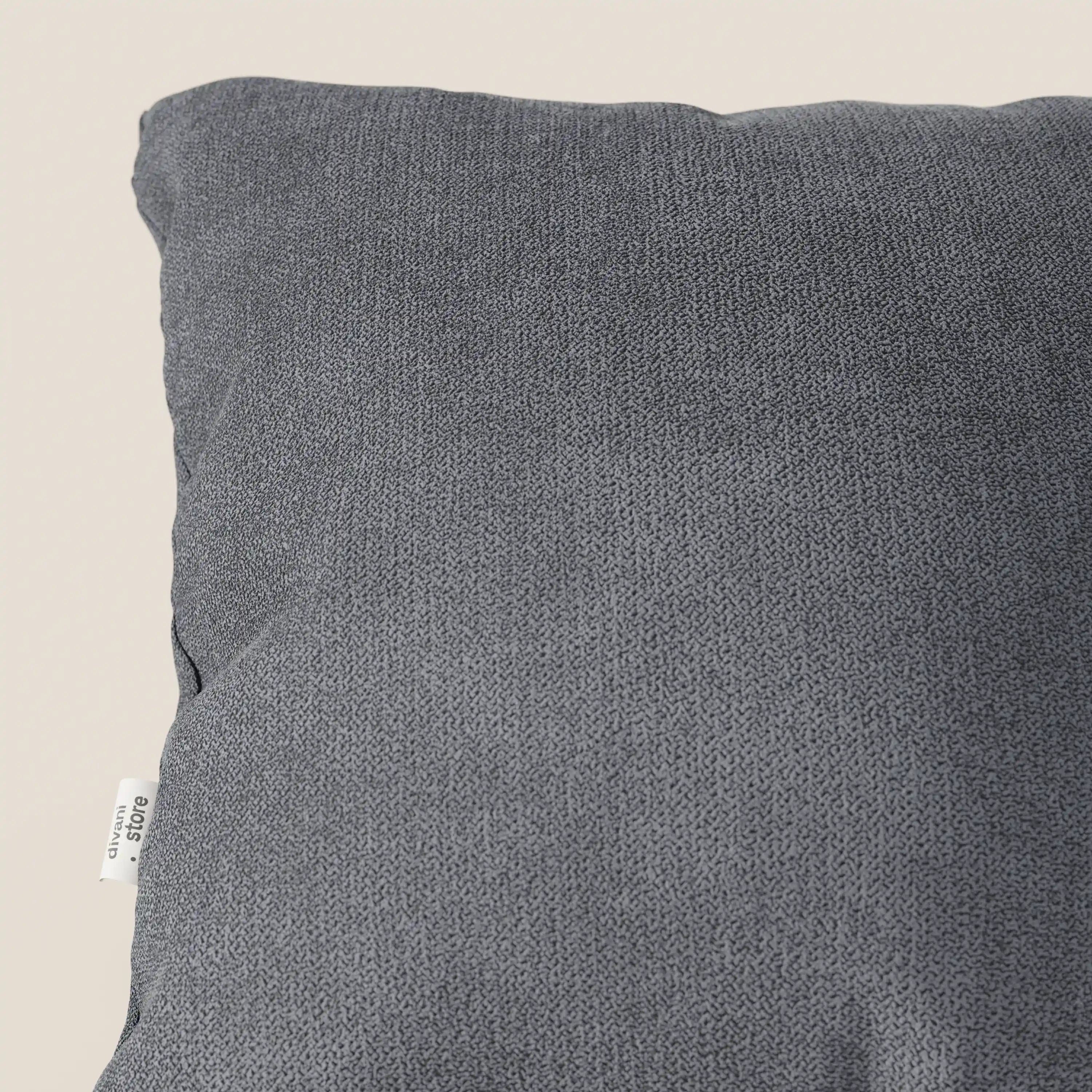 Un primo piano del cuscino Destiny di Divani.Store in morbido tessuto impermeabile T02 grigio, mostra l'angolo in alto a sinistra con una targhetta bianca; il cuscino è posizionato in diagonale su uno sfondo beige chiaro.