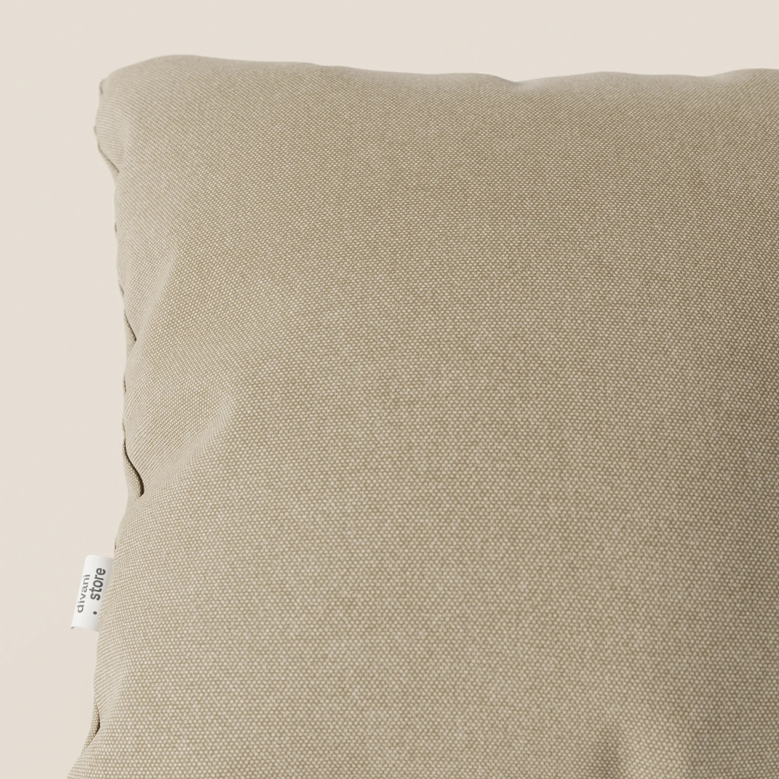 Primo piano del cuscino Honey di Divani.Store in tessuto simil cotone impermeabile T13 beige, caratterizzato da una sottile trama puntinata, bordi curvi e etichetta bianca con testo nero per un look elegante.