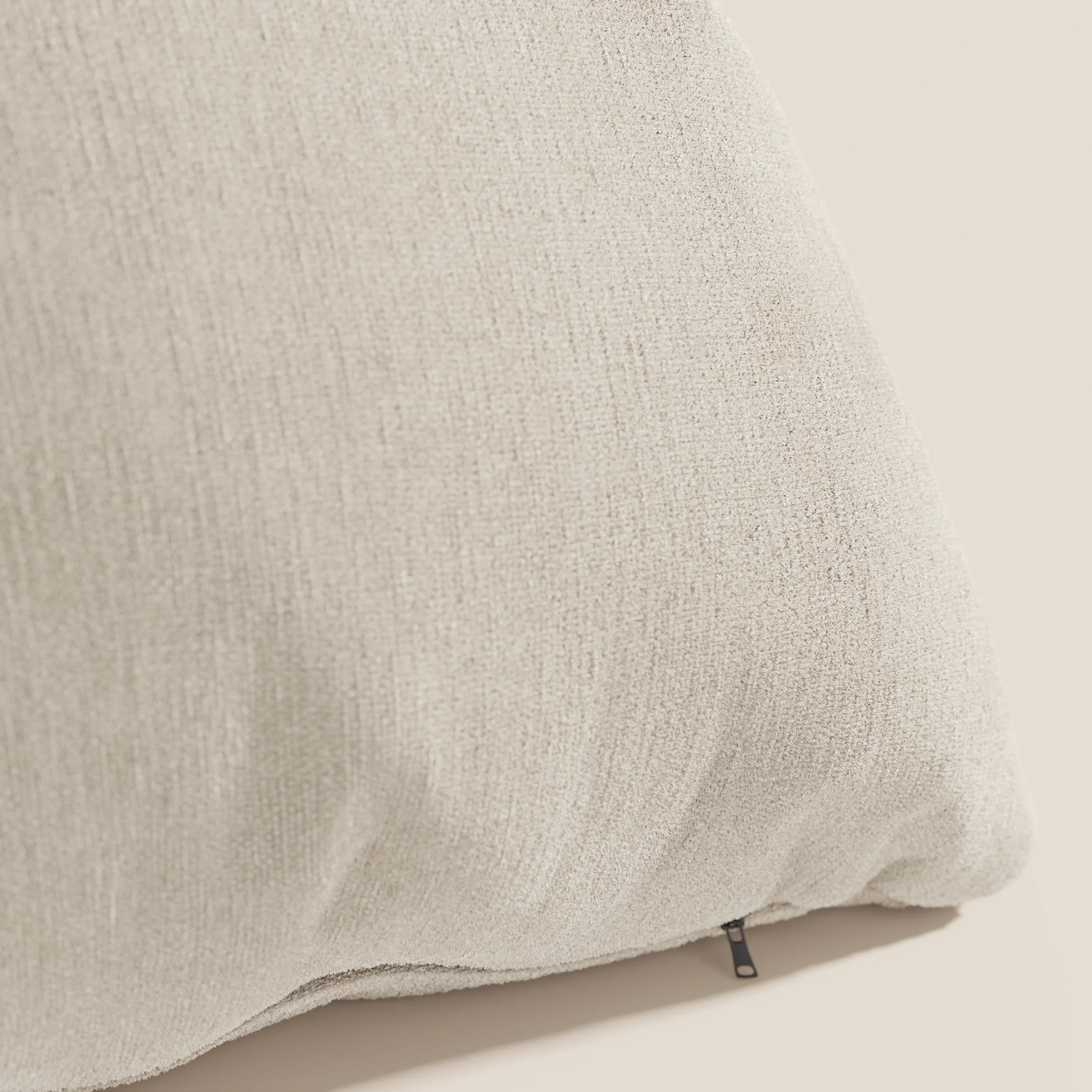 Primo piano del cuscino Bolero di Divani.Store in beige chiaro su uno sfondo neutro. Realizzato in morbido tessuto T31, resistente alle macchie, impermeabile e non restringente, presenta un sottile motivo intrecciato e una piccola cerniera nera.