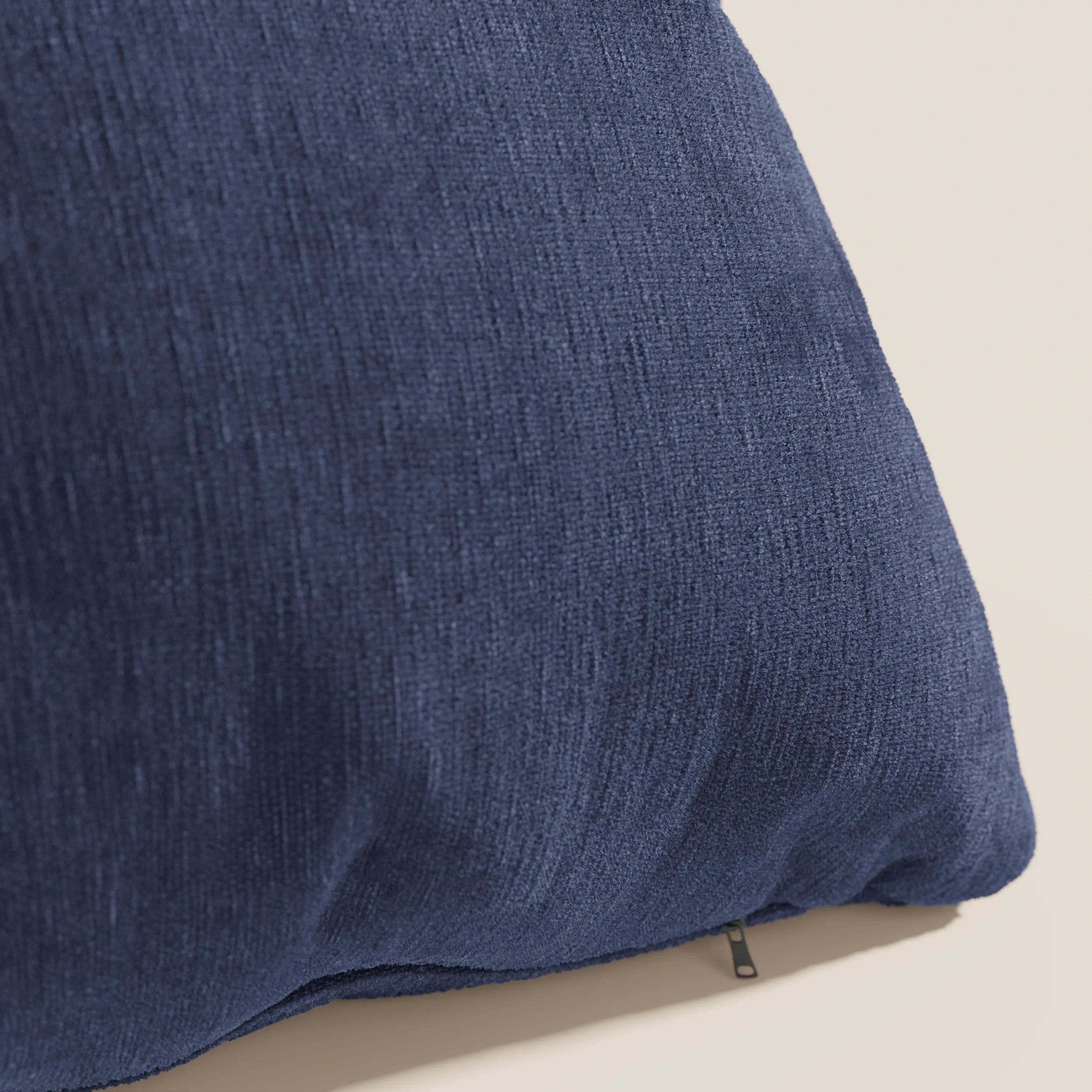 Primo piano del cuscino Bolero di Divani.Store in blu navy, caratterizzato da un morbido tessuto T31 antimacchia, impermeabile e termoretraibile. La trama fine e il piccolo tiretto della cerniera sul bordo inferiore sono visibili su uno sfondo chiaro.