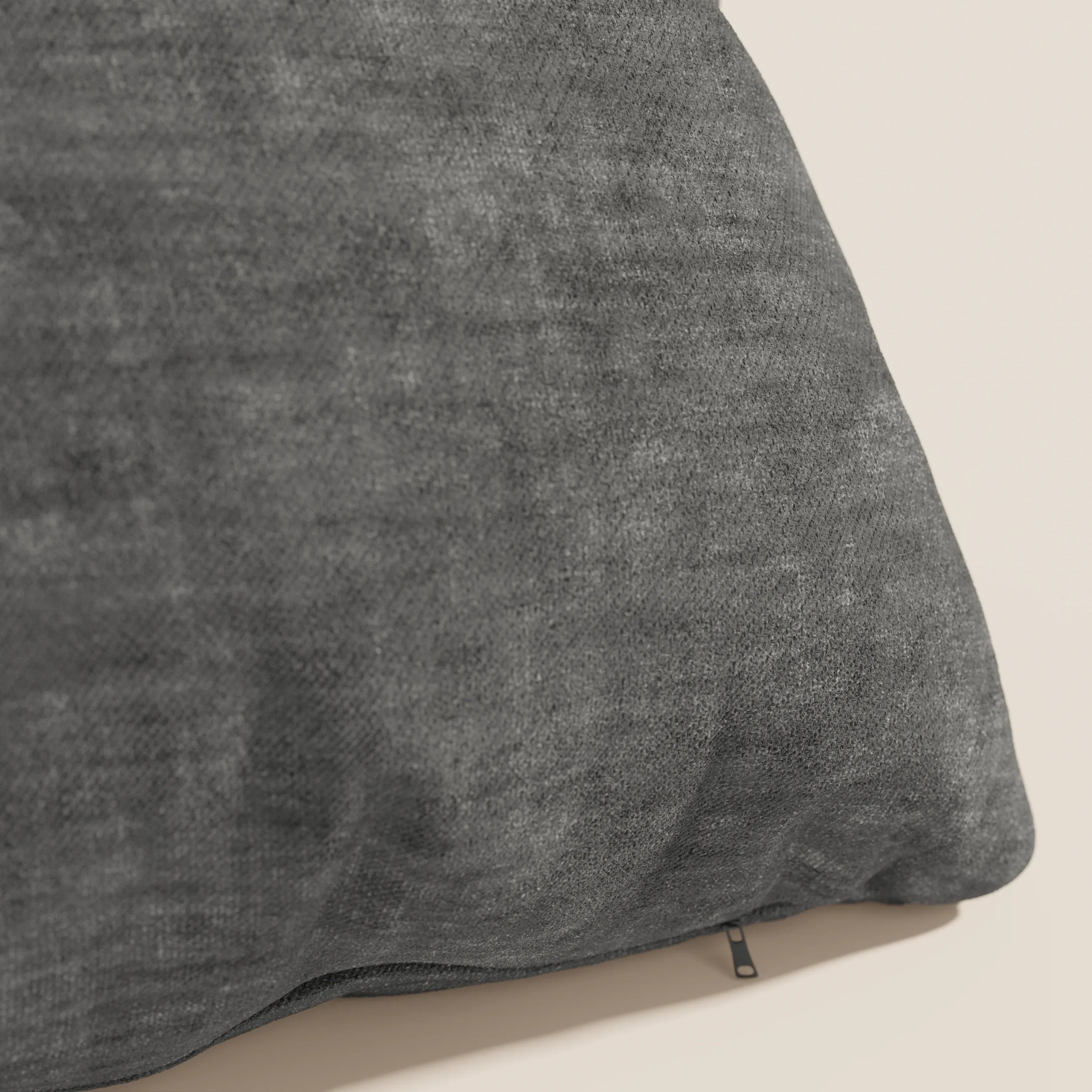 Primo piano del cuscino Sofia di Divani.Store in grigio scuro, realizzato in morbido velluto nuvolato Easy Clean T35, antimacchia e impermeabile, caratterizzato da una cerniera nera sul fondo su uno sfondo chiaro con sottili variazioni di colore.