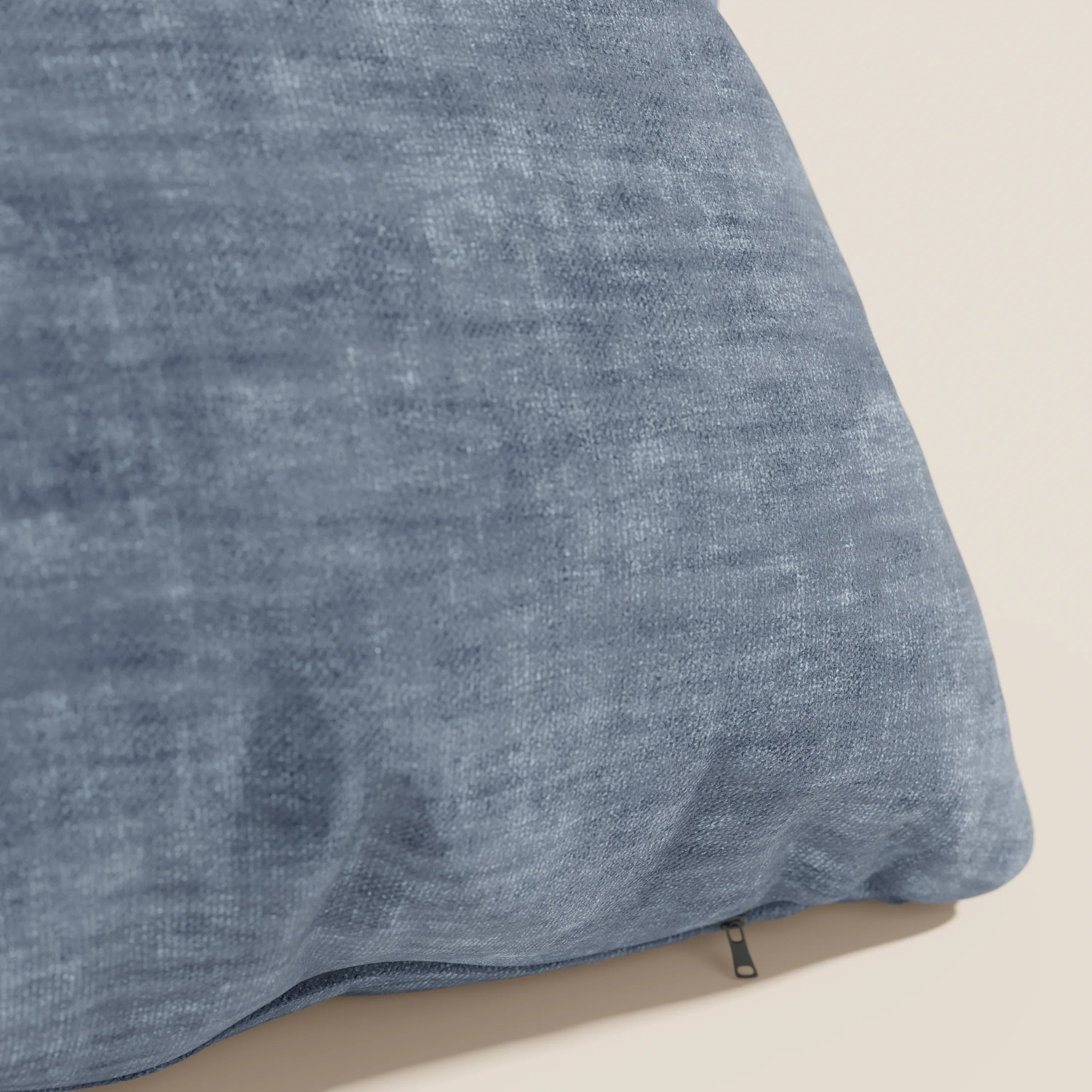 Primo piano del cuscino Sofia di Divani.Store in blu, realizzato in morbido velluto Easy Clean T35 impermeabile e antimacchia. Sottile trama, lievi pieghe e tirazip nero in basso a destra. Sfondo chiaro e solido.