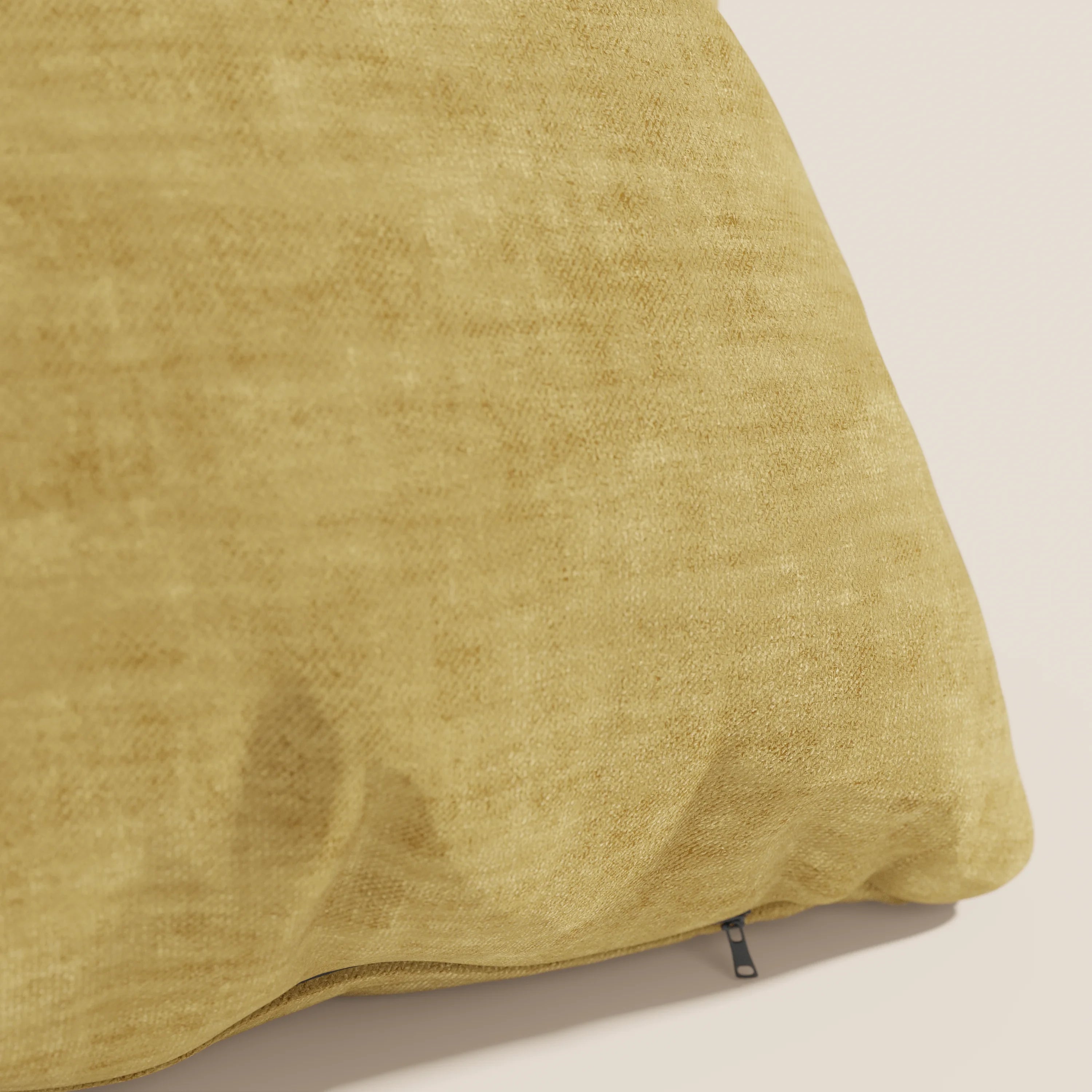 Primo piano del cuscino Sofia di Divani.Store in giallo senape, realizzato in morbido velluto Easy Clean T35 impermeabile e antimacchia. Il cuscino presenta una cerniera a vista sul fondo ed è inserito in uno sfondo bianco sporco.