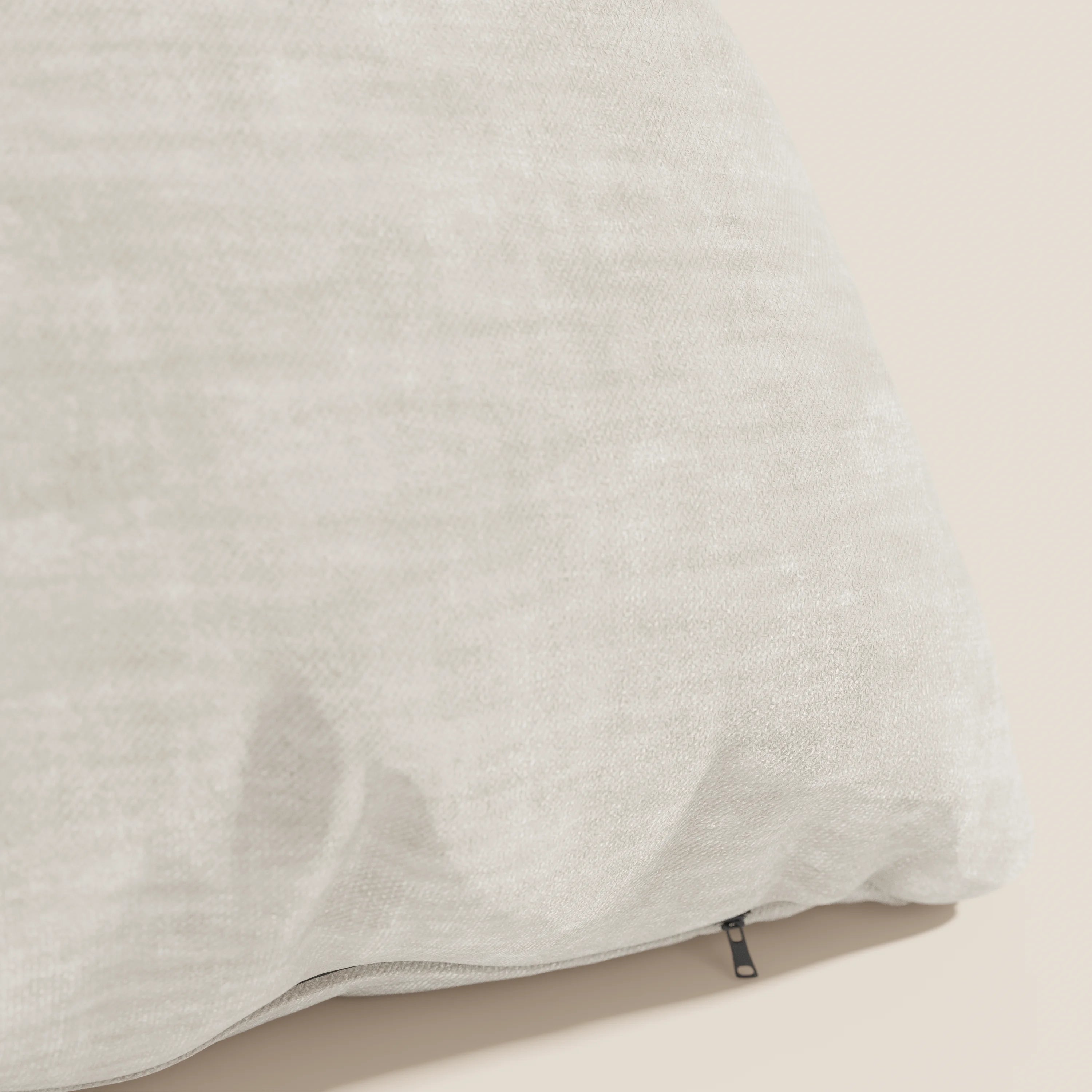 Primo piano del cuscino Sofia di Divani.Store, in velluto nuvolato beige chiaro Easy Clean T35, smacchiabile e impermeabile, caratterizzato da un sottile motivo e da una piccola cerniera nera su un bordo su uno sfondo coordinato.