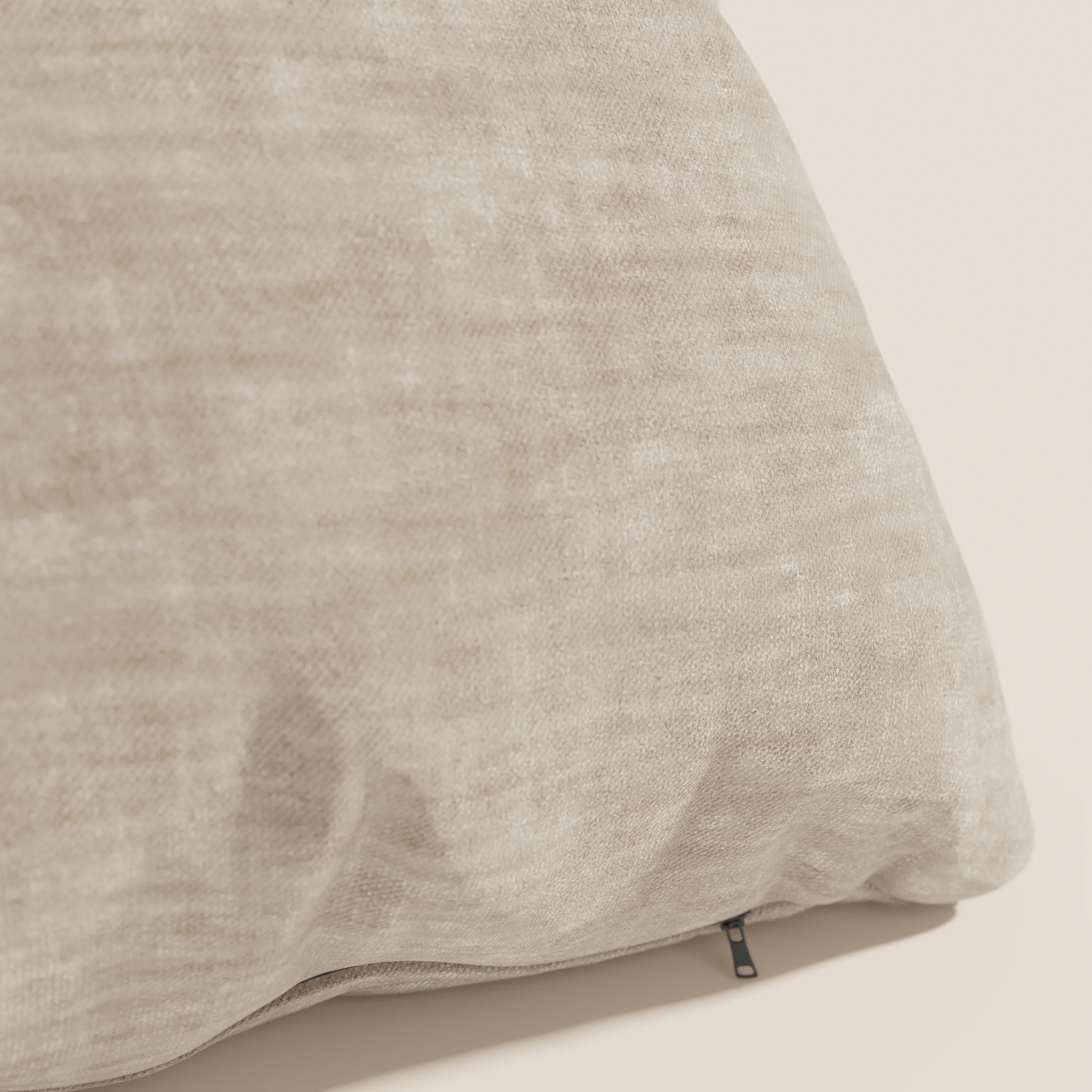 Primo piano del cuscino Sofia di Divani.Store in beige, realizzato in morbido velluto screziato Easy Clean T35, antimacchia e impermeabile. Una piccola cerniera nera è visibile su una cucitura e conferisce un aspetto accogliente e neutro.