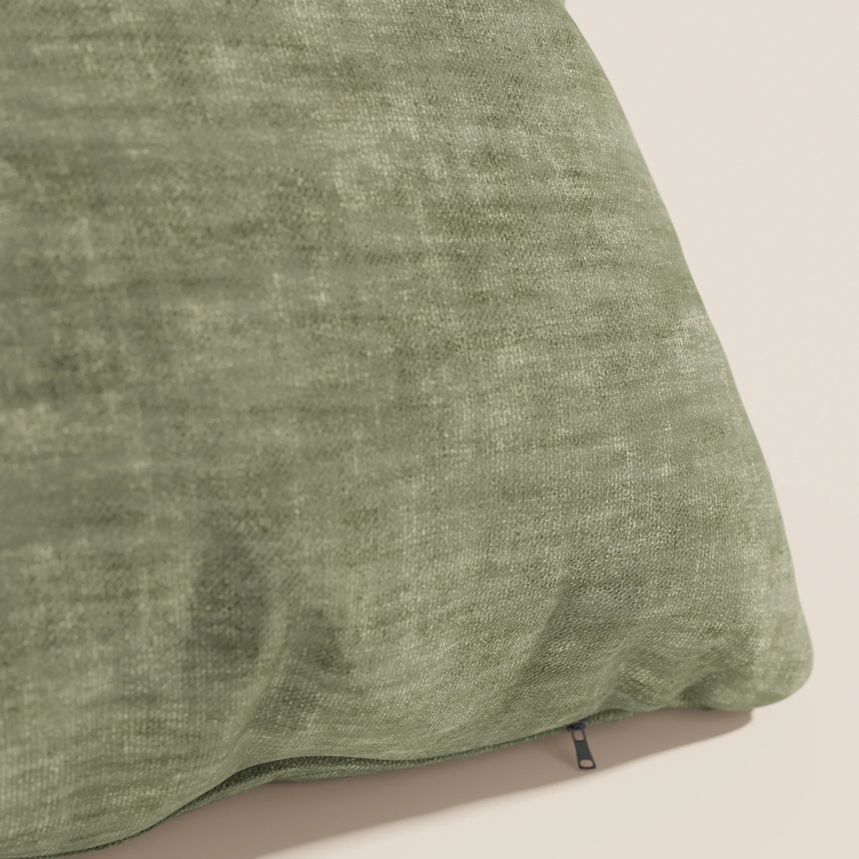 Un primo piano del cuscino Sofia di Divani.Store in velluto morbido verde nuvolato Easy Clean T35, che mostra sottili variazioni di colore e un tiretto nero vicino al bordo su uno sfondo neutro. La superficie impermeabile e antimacchia appare morbida e leggermente rugosa.