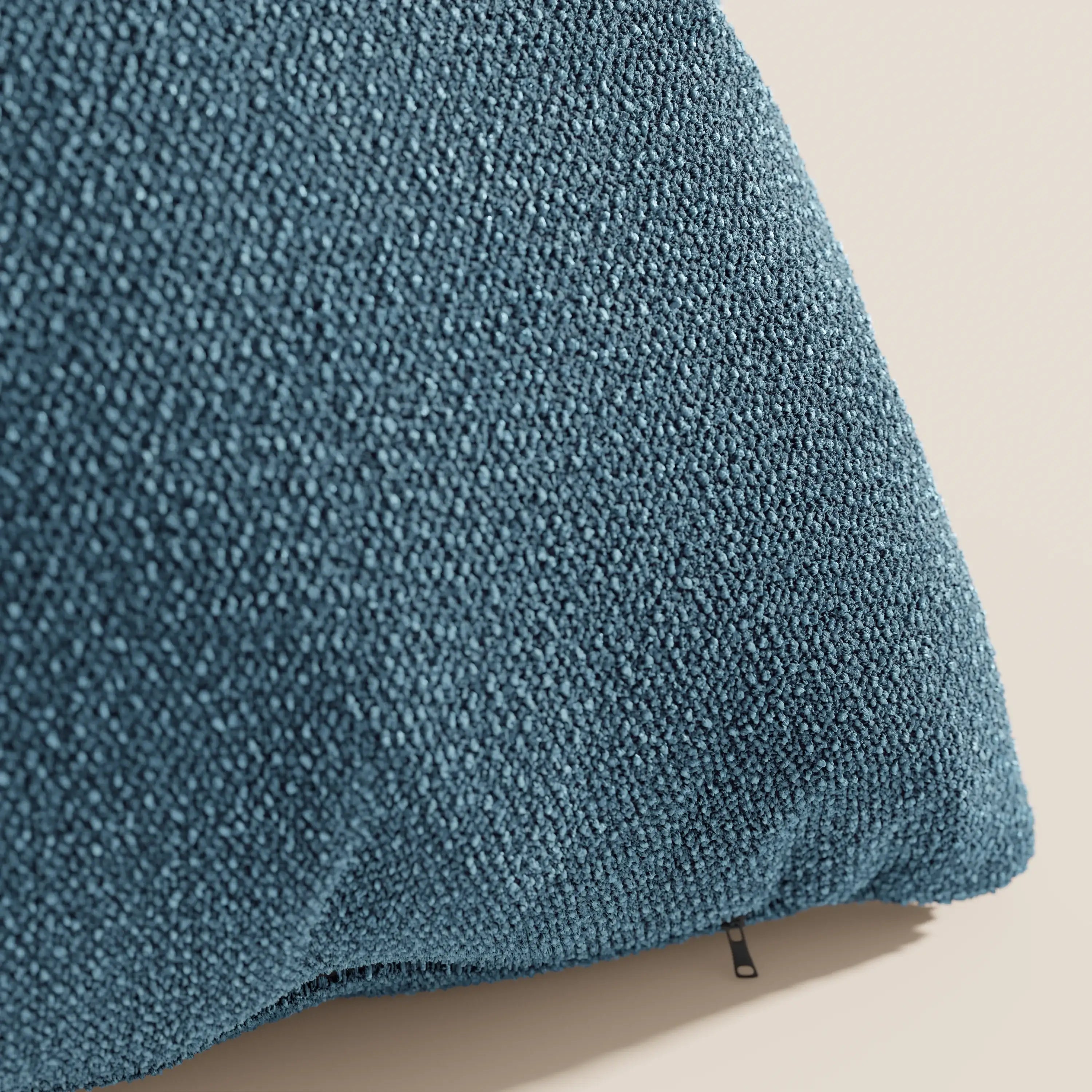Primo piano del cuscino Lambada di Divani.Store, in tessuto T33 blu, affresco, simil-cotone naturale, smacchiabile e impermeabile, su sfondo beige chiaro e con un sottile dettaglio di tirante nero.