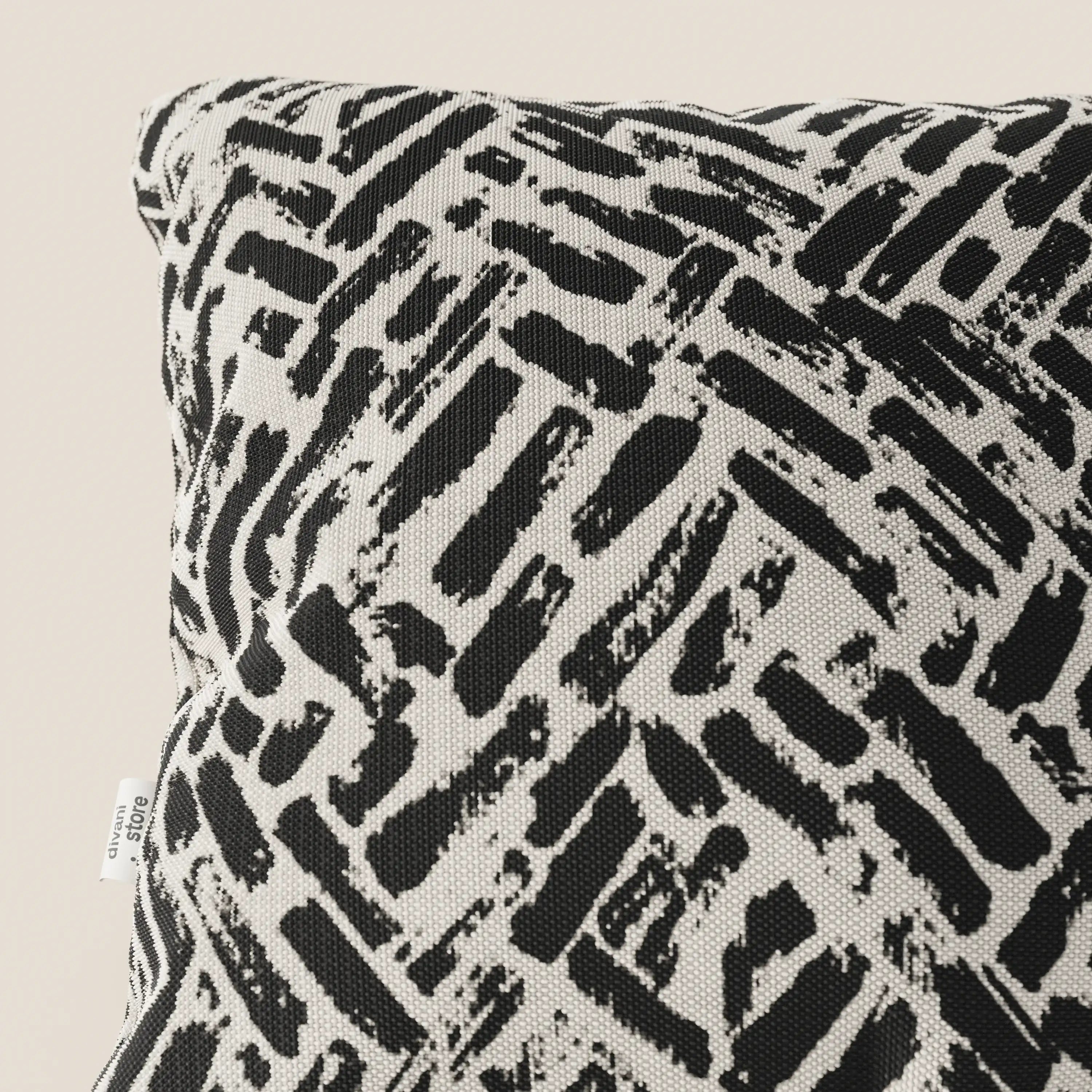 Primo piano del cuscino geometrico Brick di Divani.Store, realizzato in tessuto idrorepellente nero, con motivo astratto in bianco e nero, piccola etichetta laterale bianca, su sfondo chiaro.
