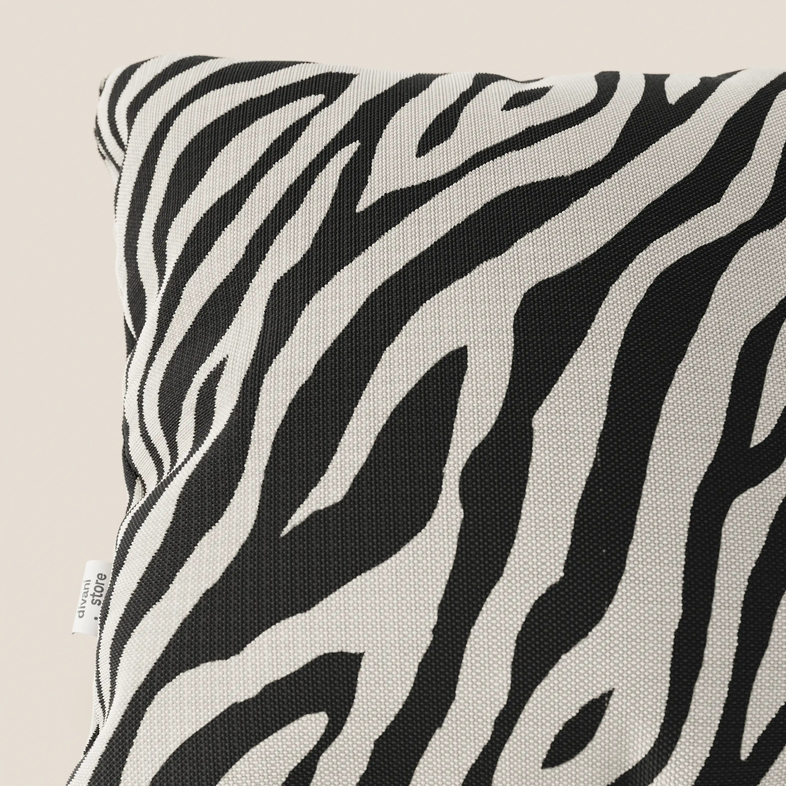 Primo piano di Divani.Store Stripe cuscini geometrici in tessuto Idrorepellente, nero, con motivo zebrato bianco e nero su sfondo beige chiaro. Sul bordo sinistro è visibile una piccola etichetta in tessuto bianco.
