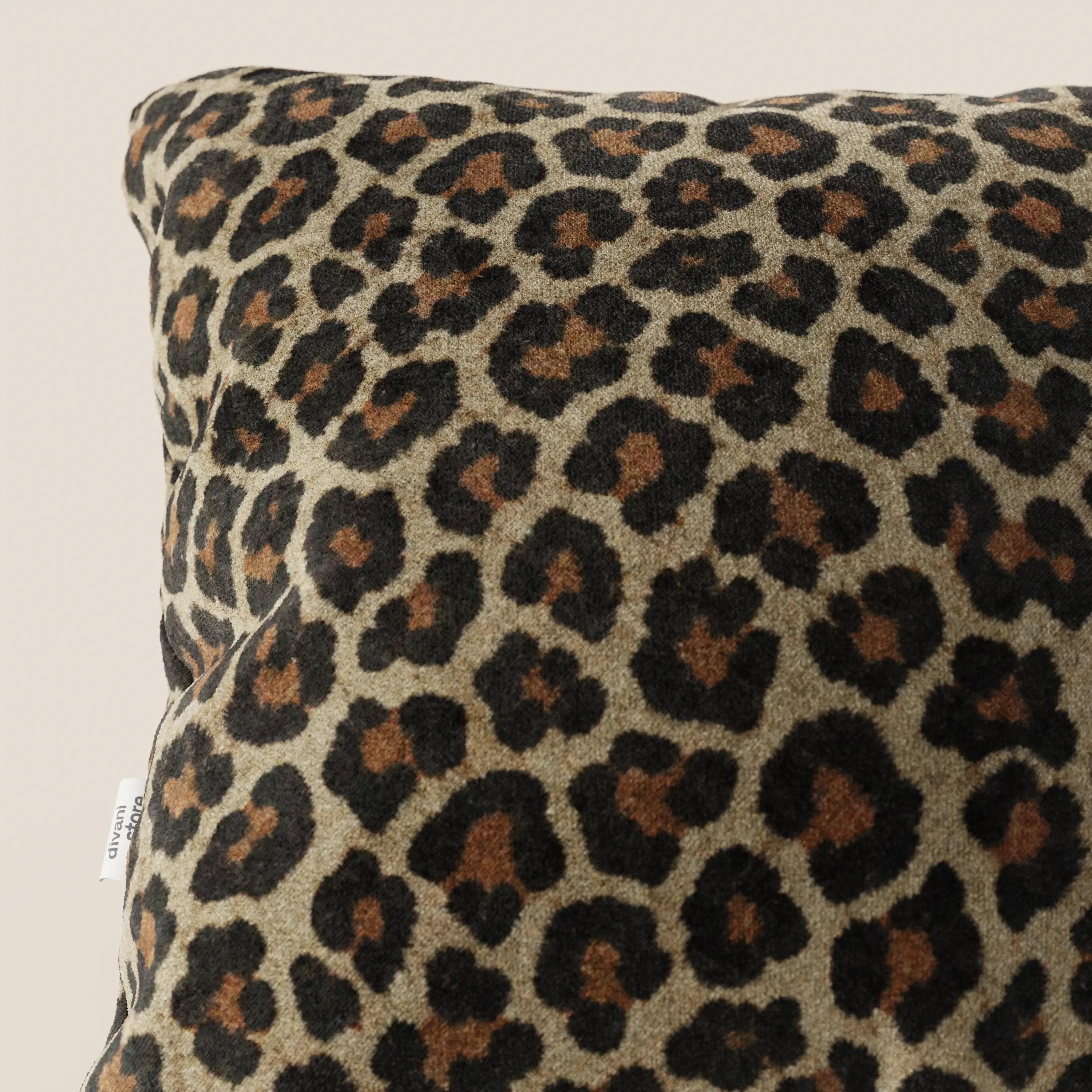 Primo piano del cuscino della collezione Wild in microfibra impermeabile leopardo di Divani.Store, caratterizzato da una stampa leopardata con macchie nere e marroni su sfondo marrone, una piccola etichetta laterale e uno sfondo neutro.