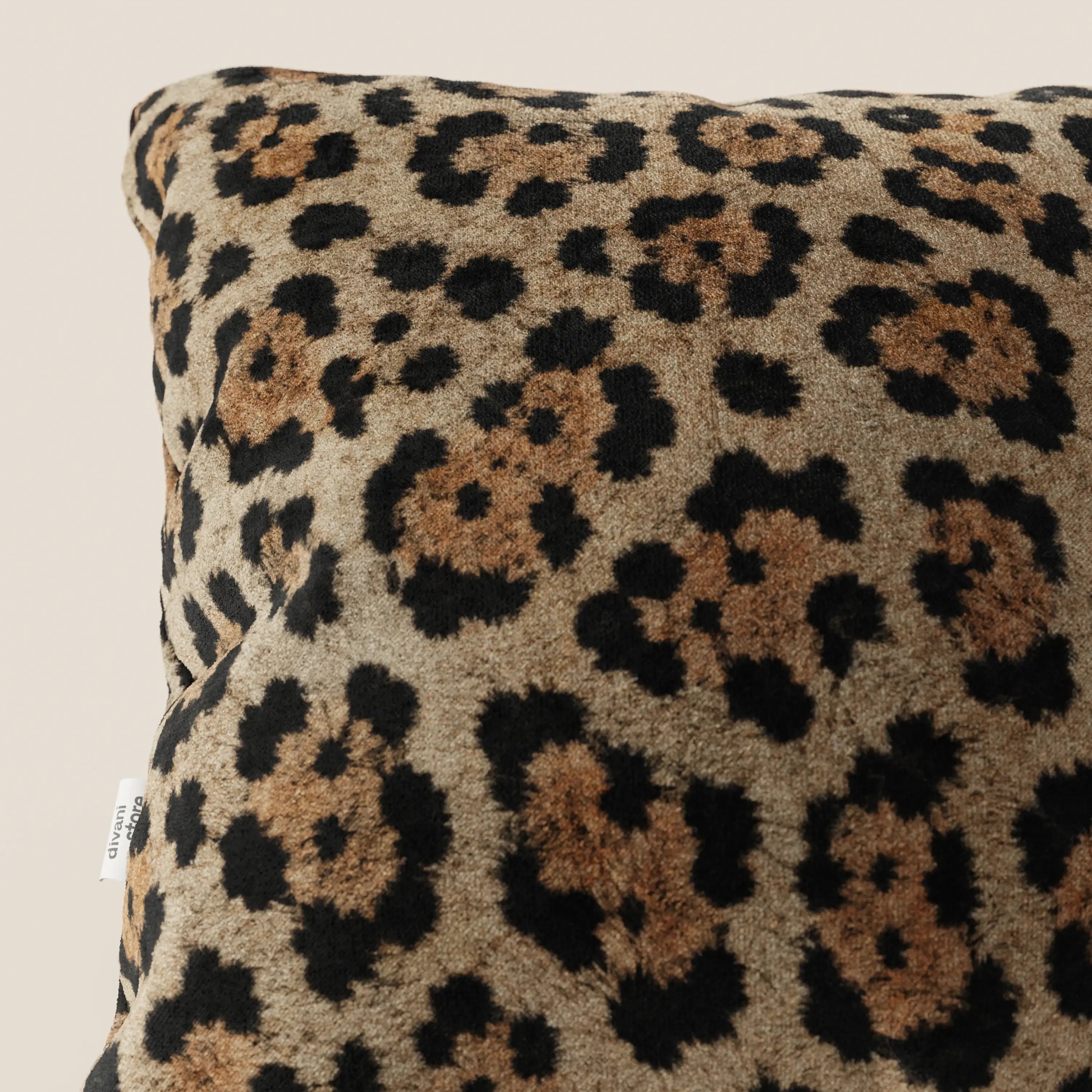 Primo piano del cuscino Divani.Store Wild in collezione Wild in microfibra impermeabile giaguaro, caratterizzato da un morbido tessuto leopardato e da una piccola etichetta bianca sulla cucitura su uno sfondo beige chiaro.