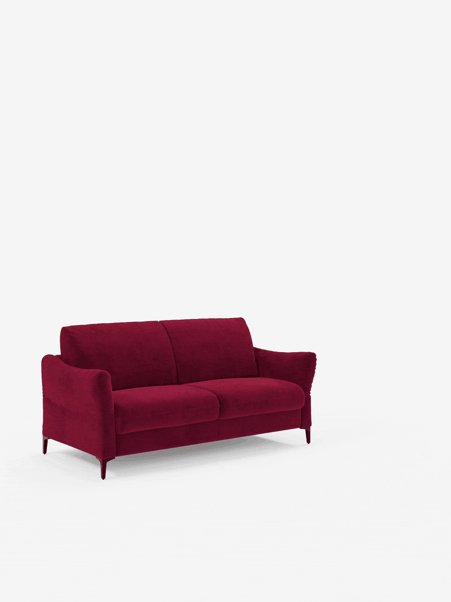 Un divano letto Dalia di Divani.Store in stile contemporaneo, rivestito in tessuto T30 di velluto rosso intenso e resistente alle macchie, con braccioli ricurvi e gambe sottili, è posto al centro di uno sfondo bianco liscio. Il divano è dotato di due cuscini di seduta e due cuscini di schienale che gli conferiscono un aspetto morbido e accogliente. L’ambiente è minimalista e ordinato.