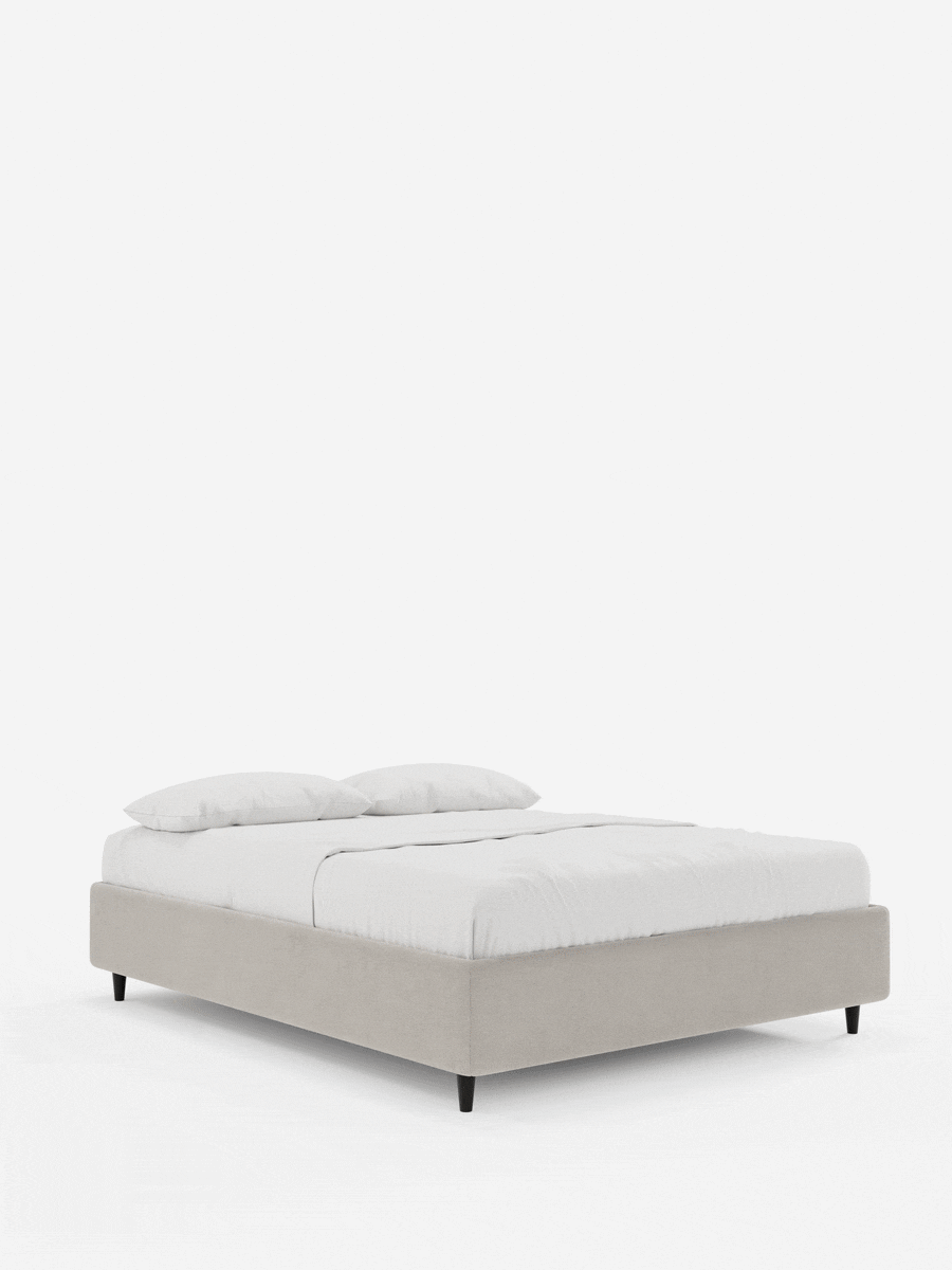 Letto a doghe imbottito ERON con contenitore in tessuto impermeabile certificato Oeko-Tex, con fianchi in tessuto beige chiaro, materasso bianco con cuscini coordinati e piedini bassi, scuri e affusolati, il tutto su uno sfondo bianco a tinta unita.