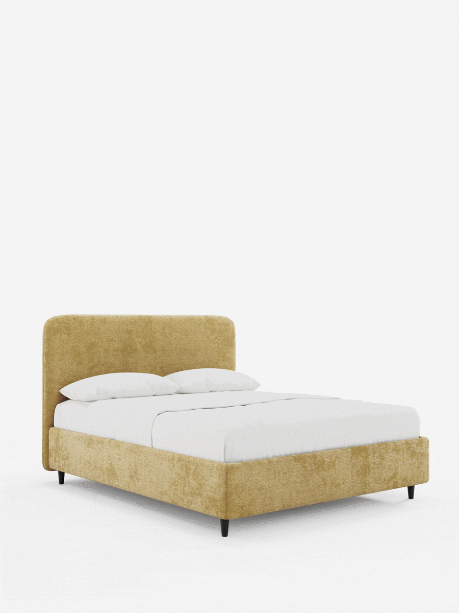 KAELOS, letto imbottito in stile minimalista - contenitore, gambe alte e testiera arrotondata in tessuto ciniglia con struttura dalla trama giallo-dorata, testiera arrotondata, due cuscini bianchi e gambe sottili scure su sfondo bianco.