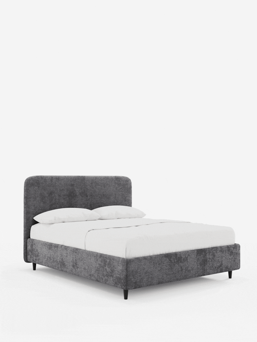 Un letto KAELOS minimal imbottito in grigio antracite, caratterizzato da una testiera arrotondata, biancheria da letto bianca, trama in tessuto e gambe corte, scure e affusolate, su uno sfondo bianco a tinta unita.