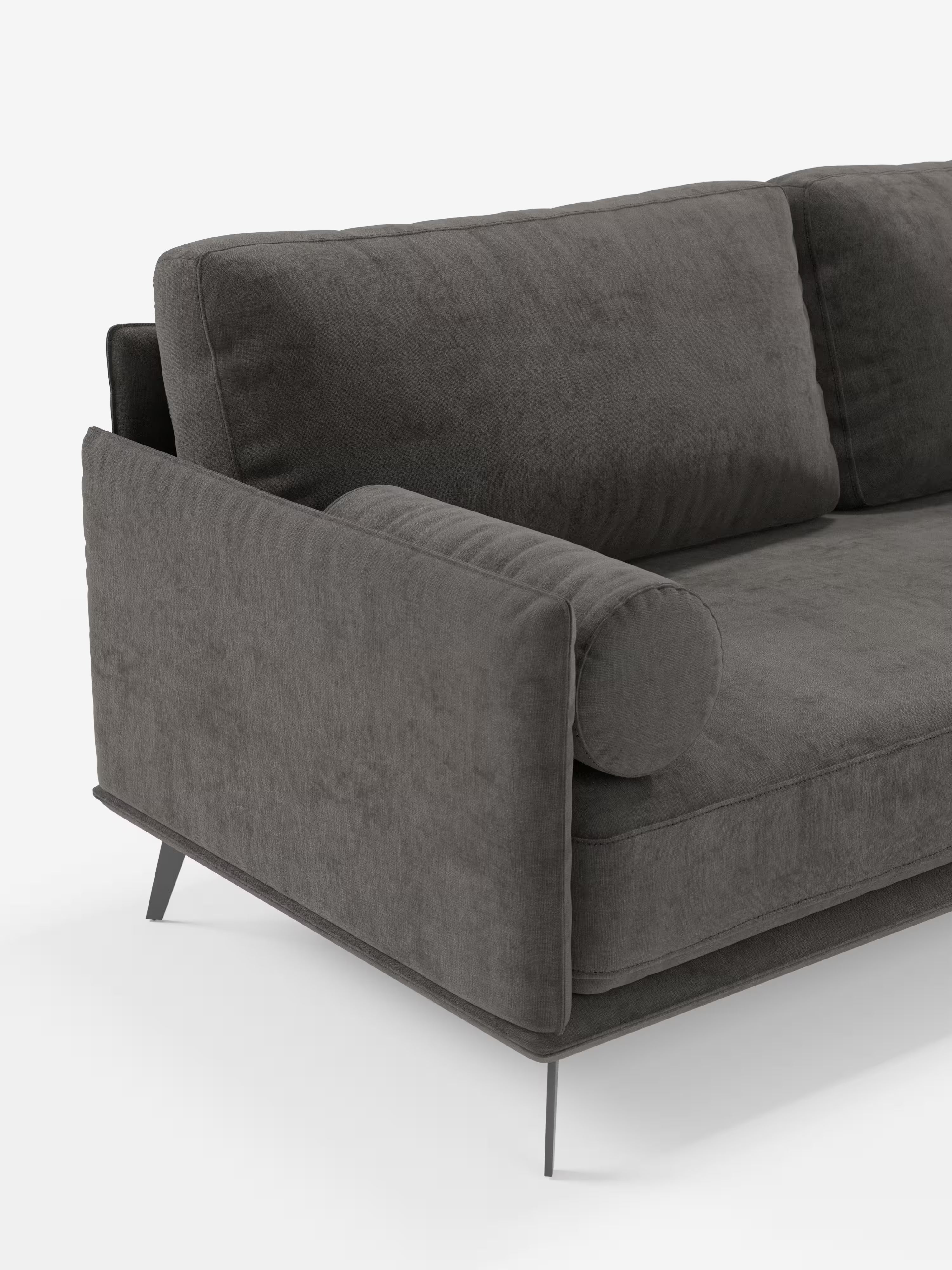 Un primo piano del divano moderno angolare con penisola “Basalto” di Divani.Store, realizzato in tessuto T31 grigio scuro e resistente alle macchie. Questo divano moderno angolare presenta un cuscino dello schienale rettangolare, un cuscino cilindrico coordinato e sottili gambe in metallo. I suoi morbidi cuscini imbottiti in piuma esaltano la superficie soffice e accogliente, che risalta sullo sfondo bianco a tinta unita.