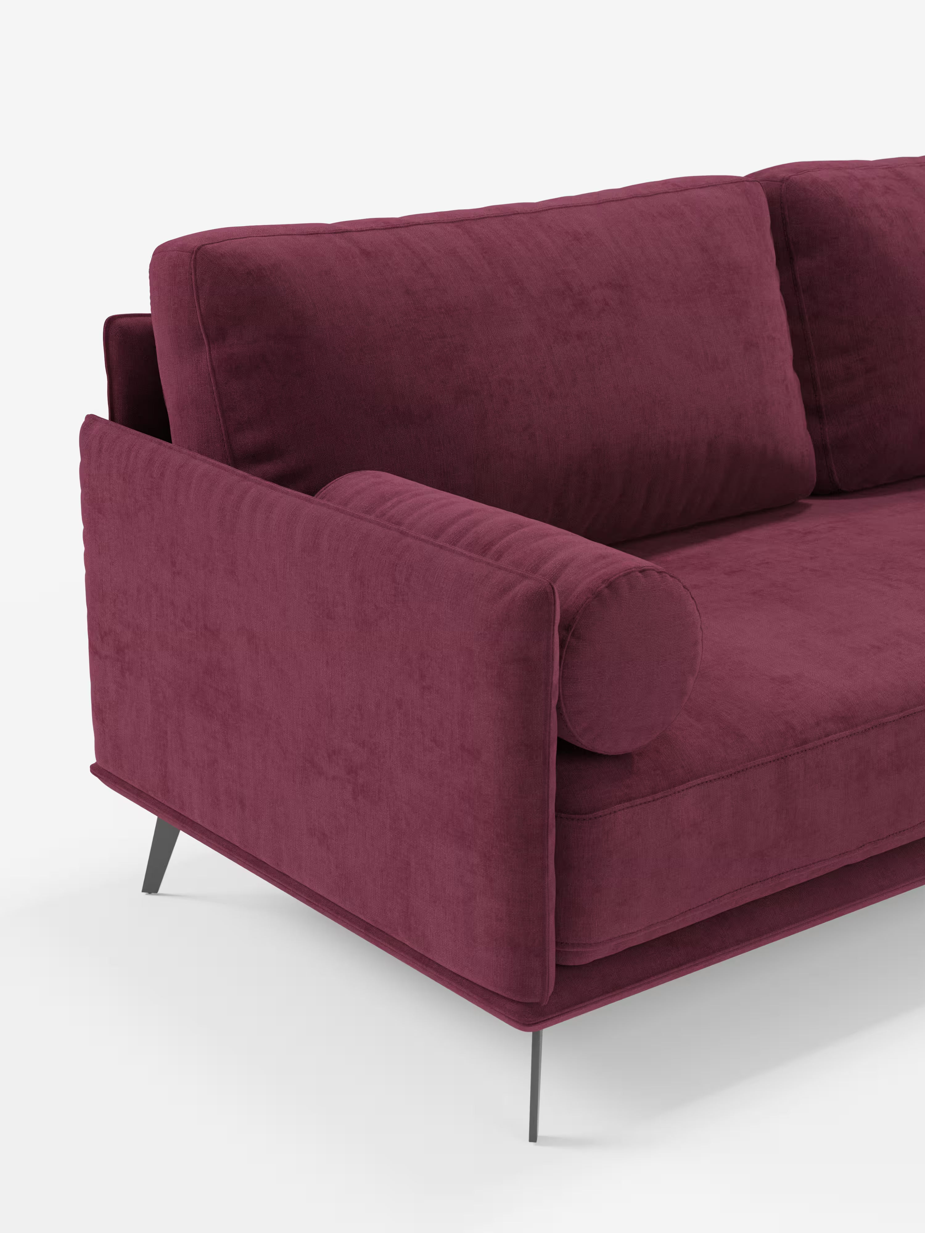 Un divano moderno angolare con penisola della linea Basalto di Divani.Store, rivestito in velluto T31 color bordeaux scuro resistente alle macchie, caratterizzato da una base sottile in metallo nero angolare, morbidi cuscini quadrati in piuma e un cuscino cilindrico sul bracciolo. Immagine su sfondo bianco a tinta unita, in cui è visibile solo il lato sinistro del divano.