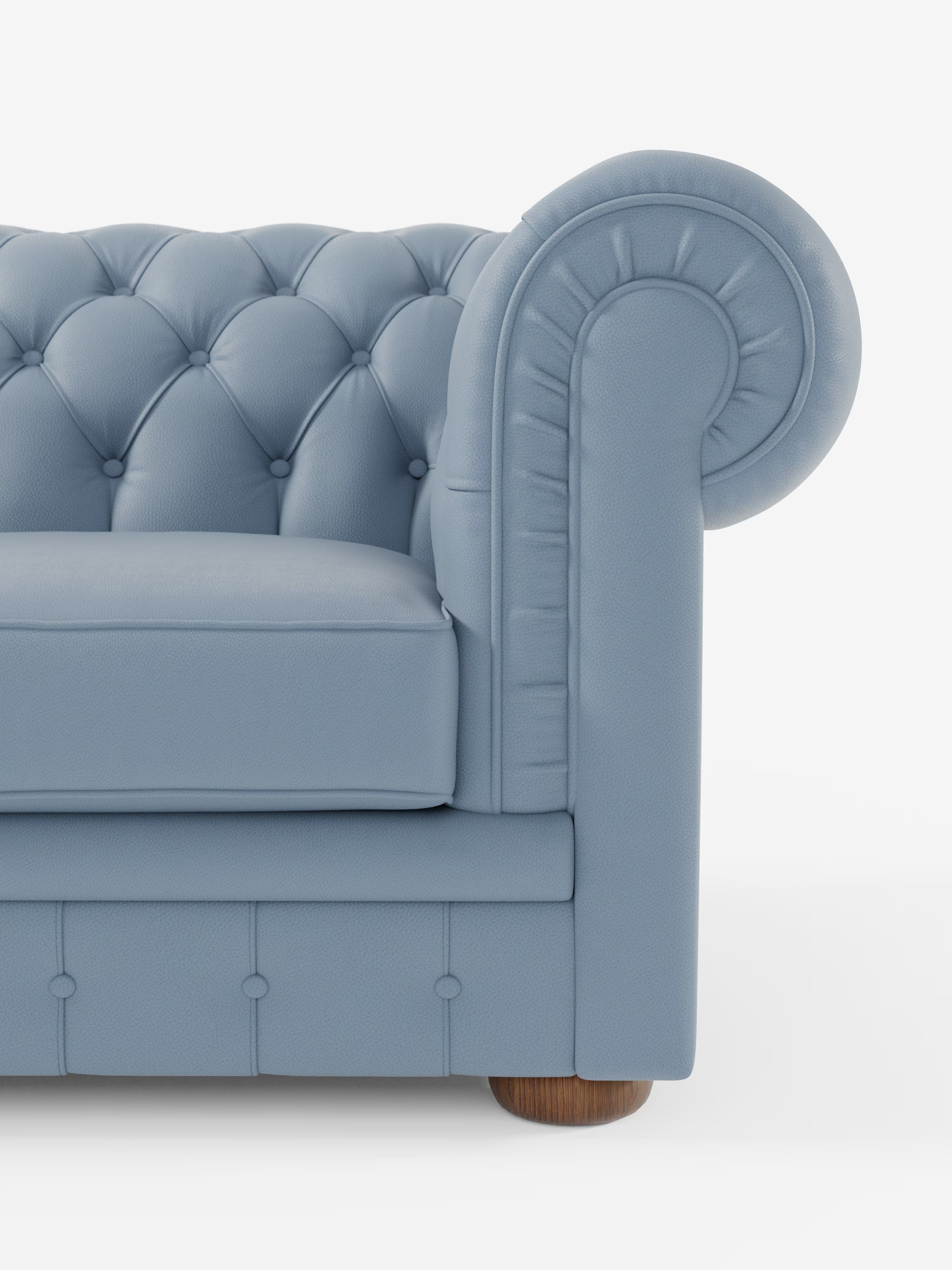Un primo piano del divano Chester 4 Posti 3 sedute in Vera Pelle – Chesterfield Capitonné Artigianale di Divani.Store, realizzato in vera pelle italiana. L'immagine mette in risalto lo schienale blu trapuntato del divano, i braccioli arrotondati e plissettati e le gambe in legno. Su uno sfondo bianco è visibile solo il lato destro di questo Chesterfield artigianale.
