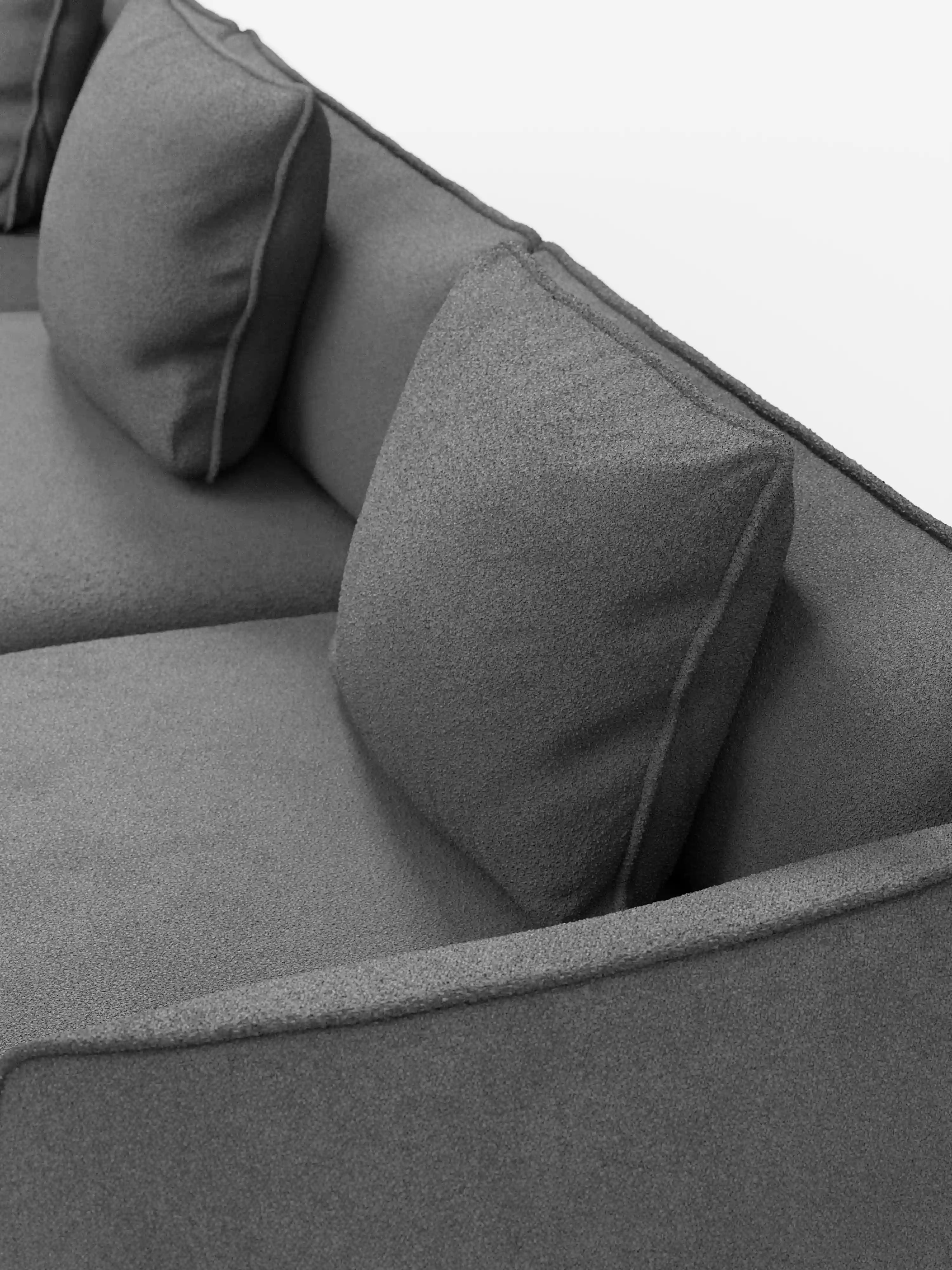 Primo piano del divano modulare a 3 posti “Nimbus” di Divani.Store, rivestito in morbido tessuto T33 effetto cotone, resistente alle macchie, in una moderna tonalità di grigio. Il divano presenta linee pulite e due cuscini quadrati abbinati, ripresi da un’angolazione dall’alto per evidenziarne la texture liscia e i dettagli dei cuscini della seduta e dello schienale su uno sfondo a tinta unita.