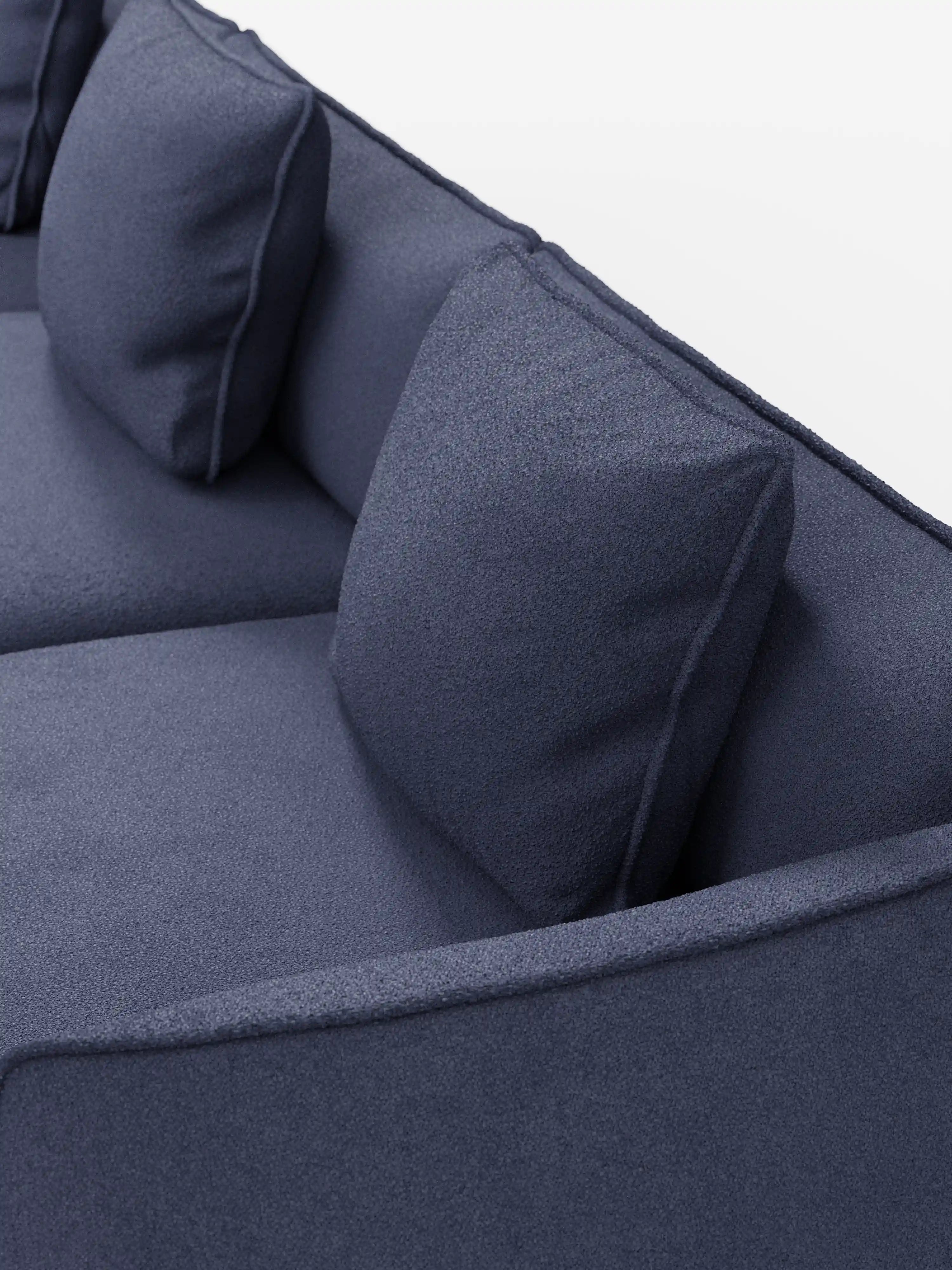Un primo piano del divano modulare a 3 posti “Nimbus” di Divani.Store, realizzato in tessuto effetto cotone blu scuro, testurizzato e resistente alle macchie, con due cuscini quadrati per lo schienale, su uno sfondo bianco a tinta unita.