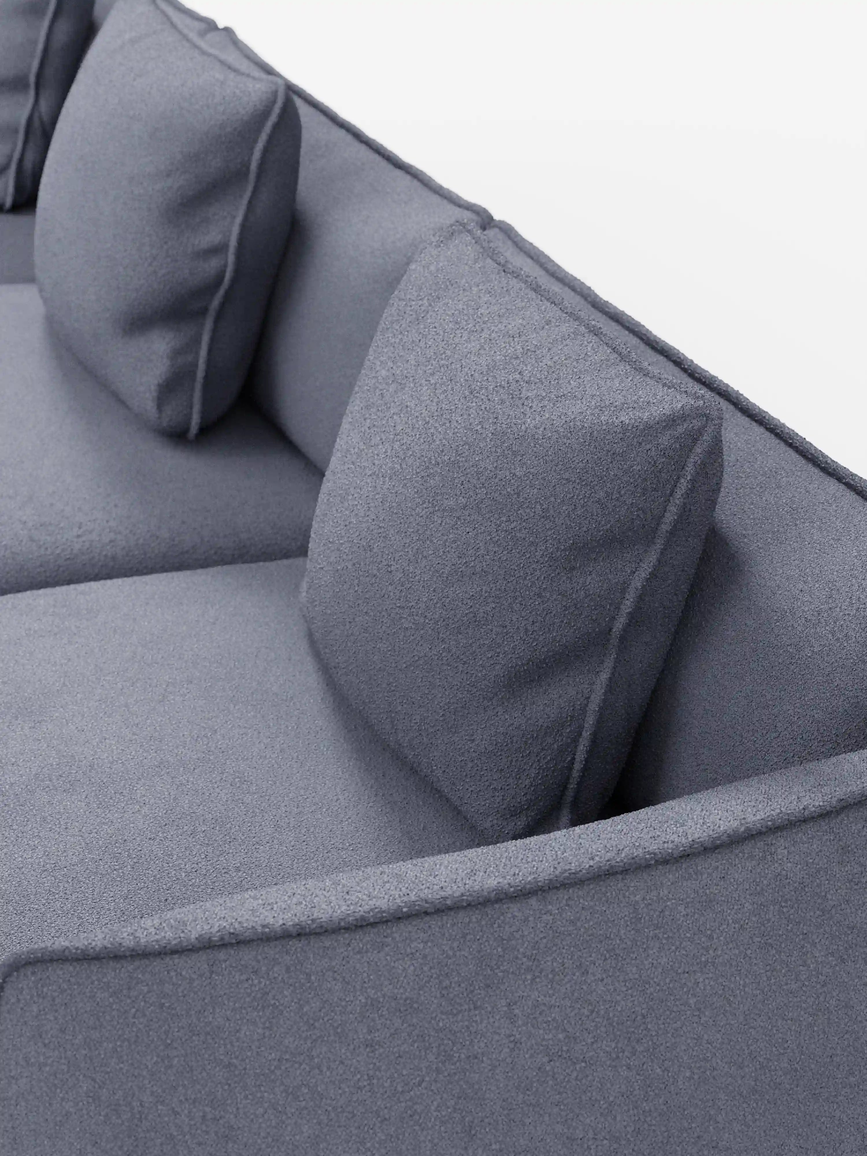 Un primo piano del divano modulare a 3 posti “Nimbus” di Divani.Store, rivestito in morbido tessuto T33 effetto cotone resistente alle macchie. Il moderno design grigio presenta due cuscini di seduta e due cuscini quadrati abbinati con una finitura leggermente testurizzata. I braccioli e lo schienale a vista creano un look pulito e minimalista sullo sfondo bianco a tinta unita.
