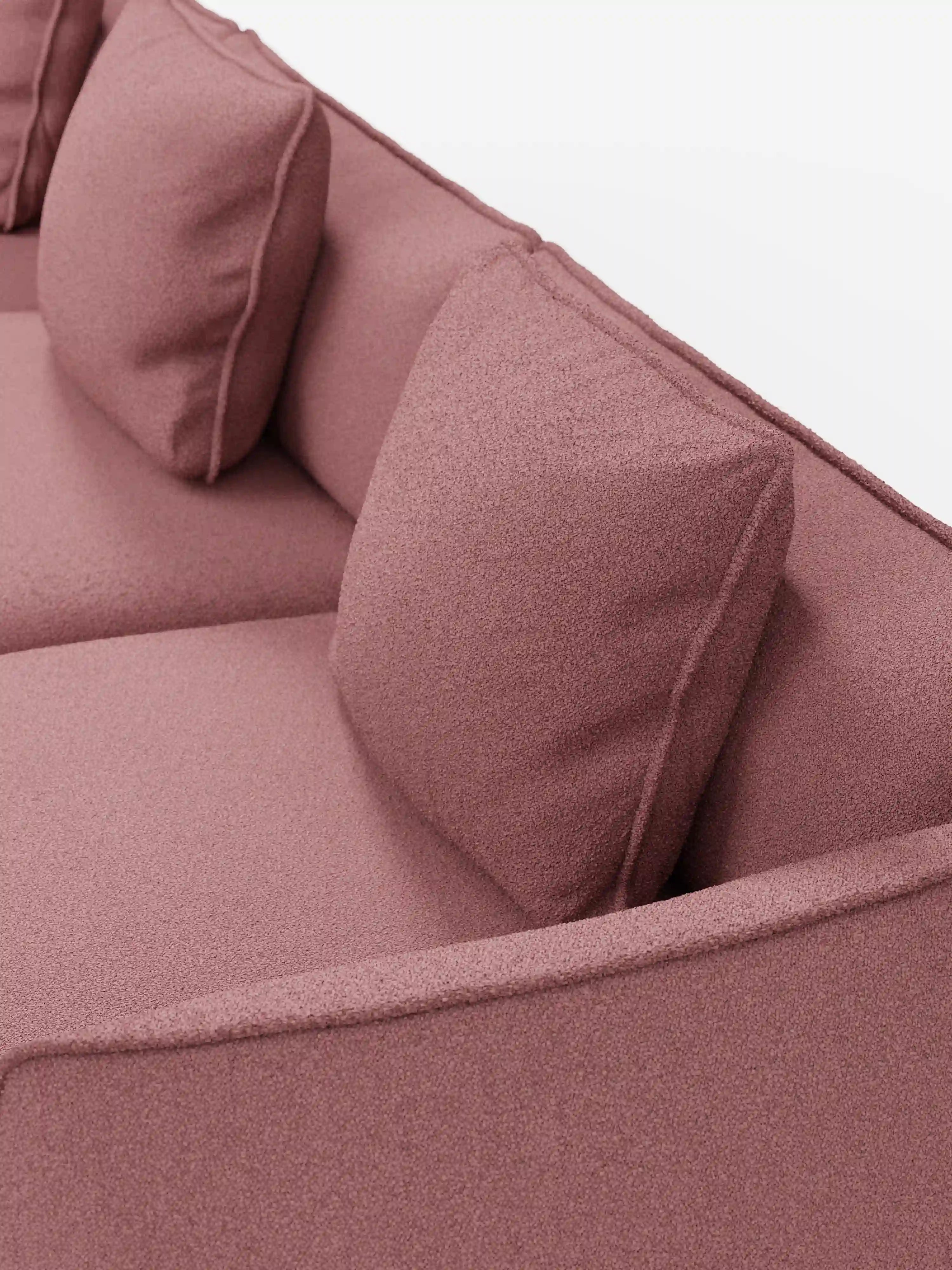 Un primo piano del divano modulare a 3 posti Nimbus di Divani.Store, rivestito in tessuto T33 effetto cotone, morbido e resistente alle macchie, nei toni del rosa malva, con due cuscini quadrati abbinati e braccioli lisci ed eleganti su uno sfondo bianco a tinta unita.