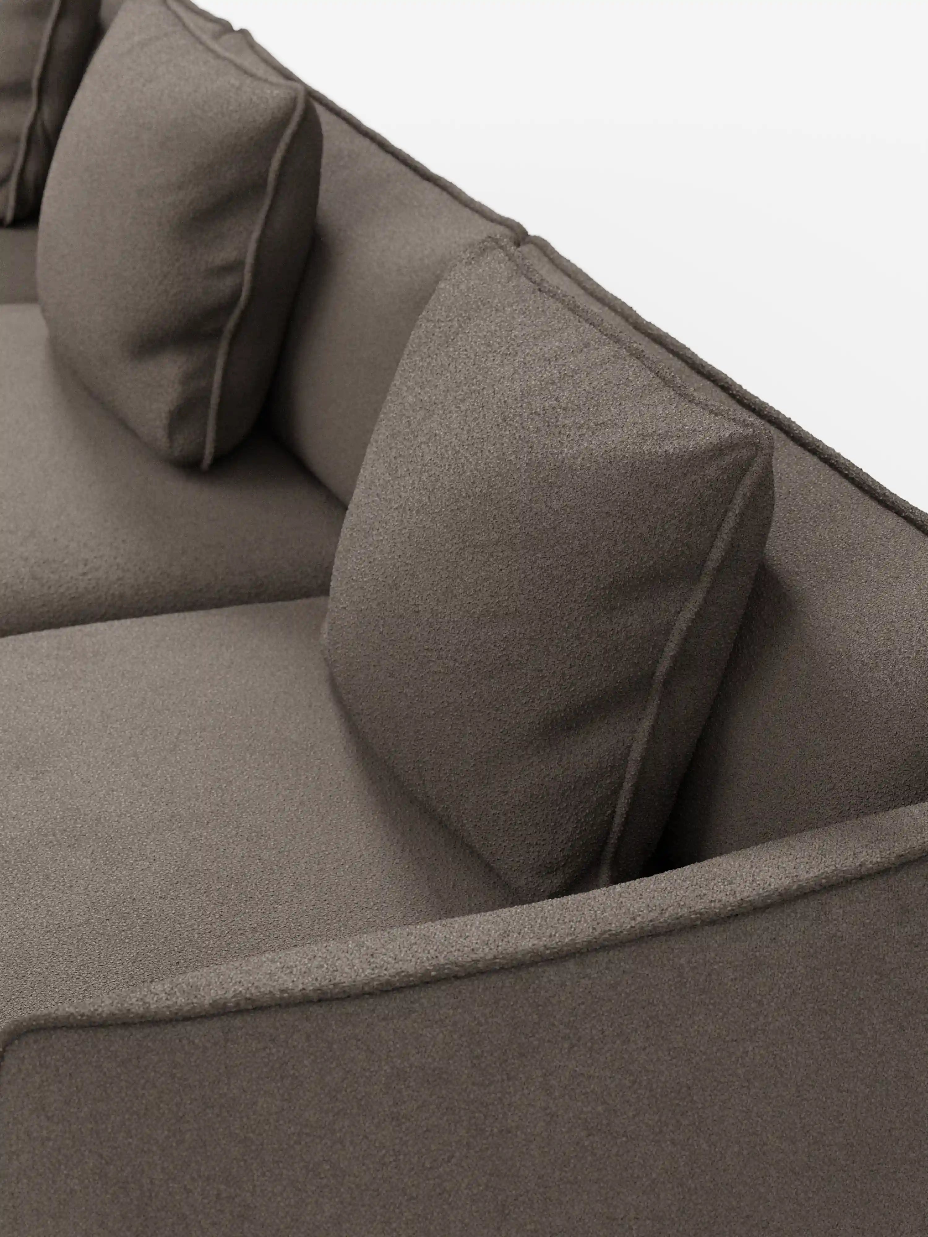 Primo piano del divano modulare a 3 posti Nimbus, realizzabile in morbido tessuto smacchiabile effetto cotone T33 di Divani.Store, qui raffigurato in un moderno tessuto marrone con due cuscini quadrati sullo schienale e una parte del bracciolo. Le linee pulite e la superficie morbida e materica mettono in risalto i soffici cuscini su uno sfondo bianco a tinta unita.