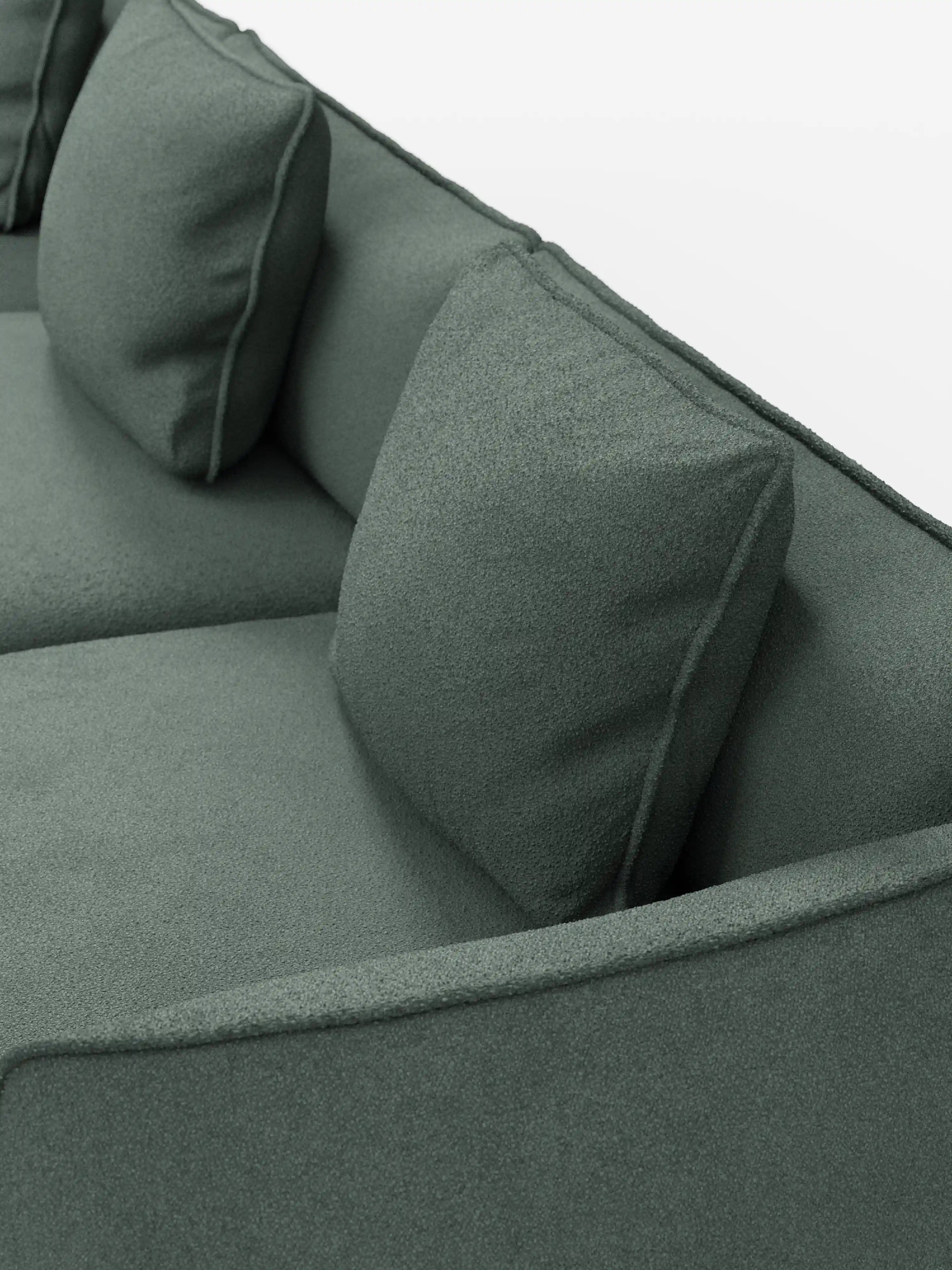 Primo piano del divano modulare a 3 posti Nimbus di Divani.Store, rivestito in un morbido tessuto verde testurizzato, resistente alle macchie, con finitura T33 effetto cotone. Due cuscini quadrati poggiano contro lo schienale, sottolineando il rivestimento morbido ma strutturato del divano e le linee pulite e minimaliste del suo design.