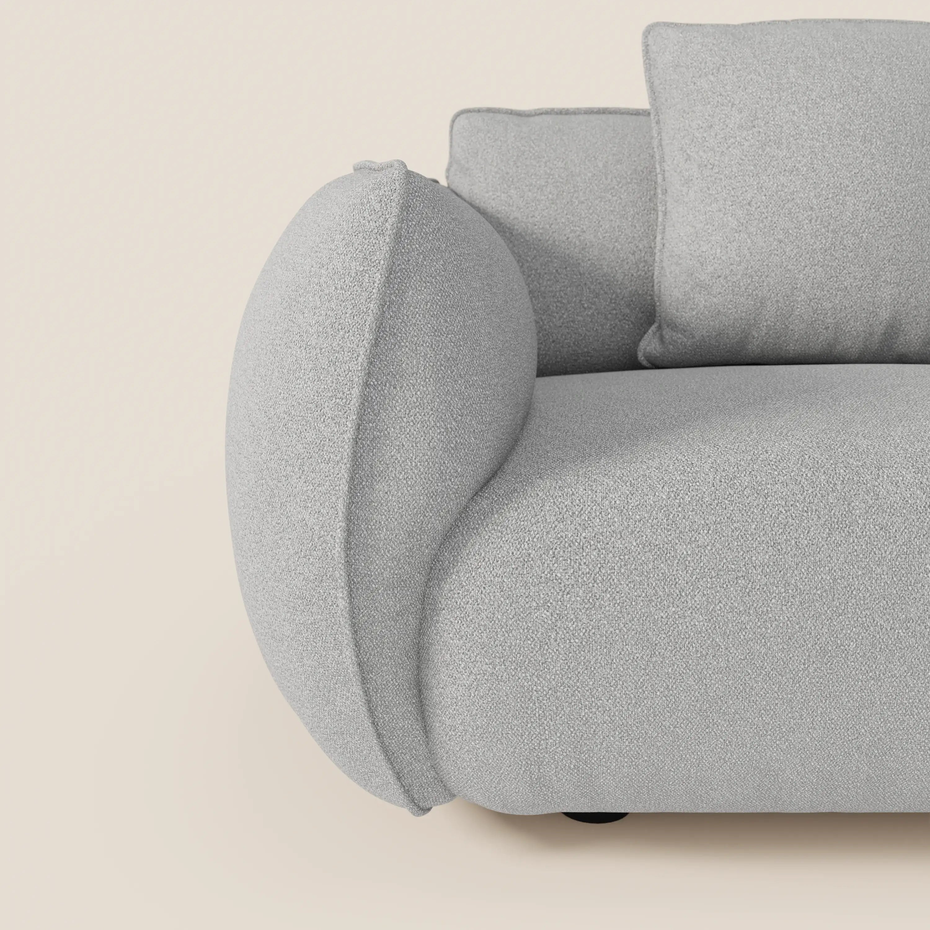 Primo piano del divano Nimbus 3 posti modulare e componibile (250 cm) di Divani.Store, caratterizzato da braccioli curvi e imbottiti e cuscini in morbido tessuto T33 antimacchia effetto cotone, su sfondo bianco sporco.
