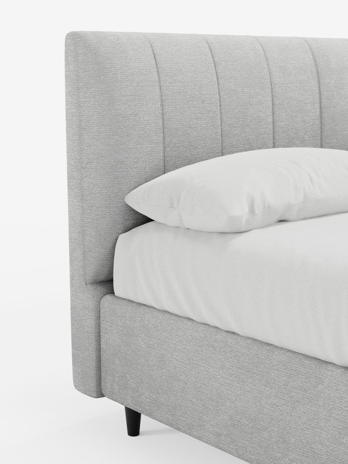 Primo piano del letto imbottito ONYX con contenitore e testiera verticale in tessuto certificato Oeko-Tex® di Letti.store. La testiera e la struttura, di colore grigio chiaro e caratterizzate da scanalature verticali, presentano un design moderno, con biancheria da letto bianca e un cuscino. Questo letto imbottito con contenitore poggia su gambe corte e affusolate di colore scuro, che risaltano sullo sfondo bianco.
